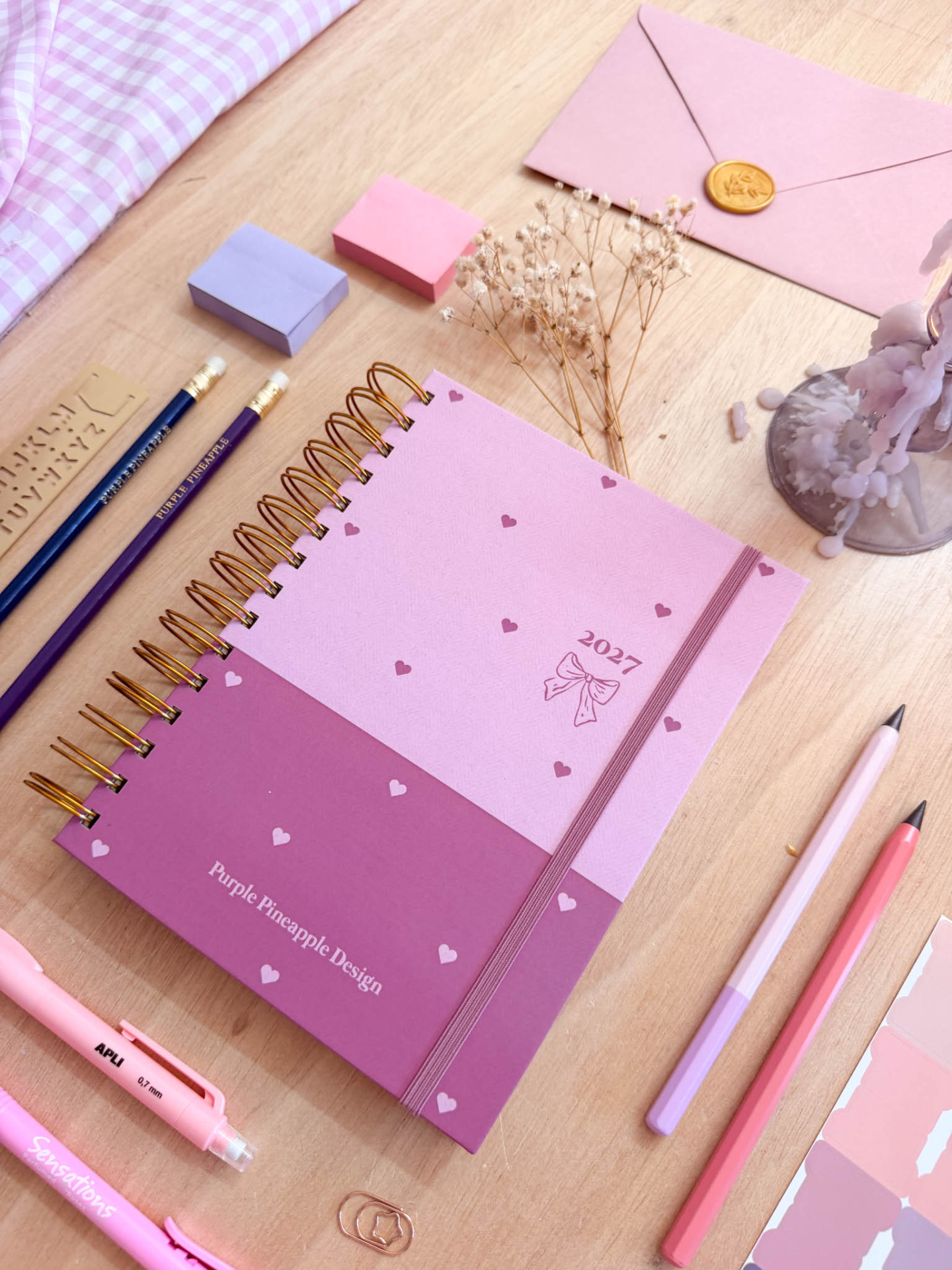 Agenda rosa com corações, lápis, caneta, envelopes com selo, blocos de notas e flores secas em superfície de madeira