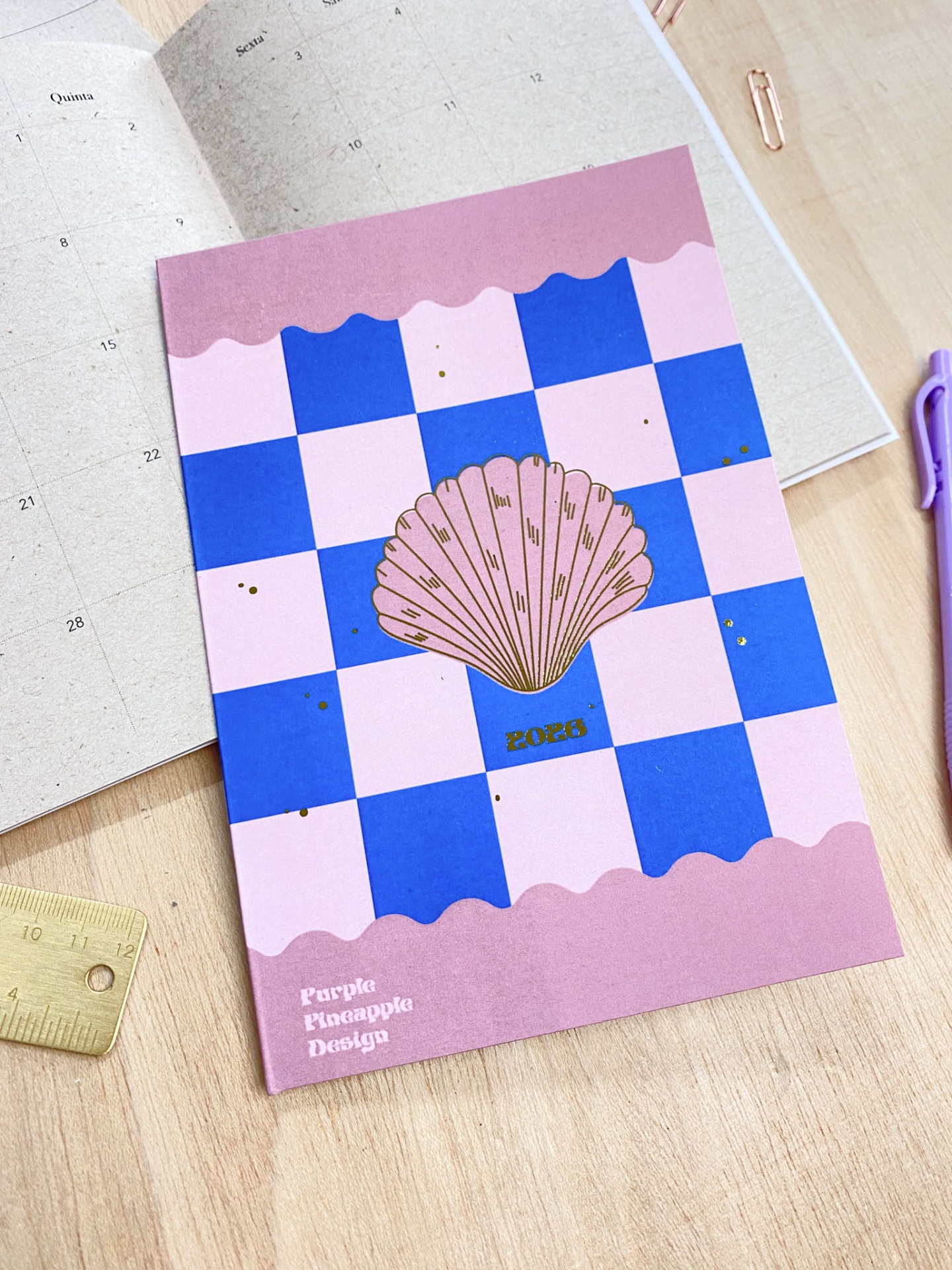 Caderno rosa e azul com concha dourada e texto 2023 sobre mesa com acessórios