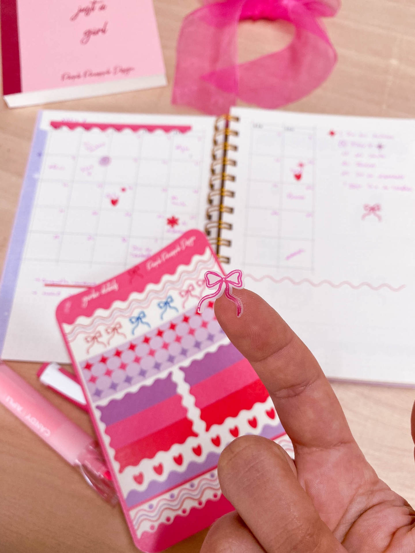 Autocolante laço rosa na ponta do dedo com diário e autocolantes ao fundo