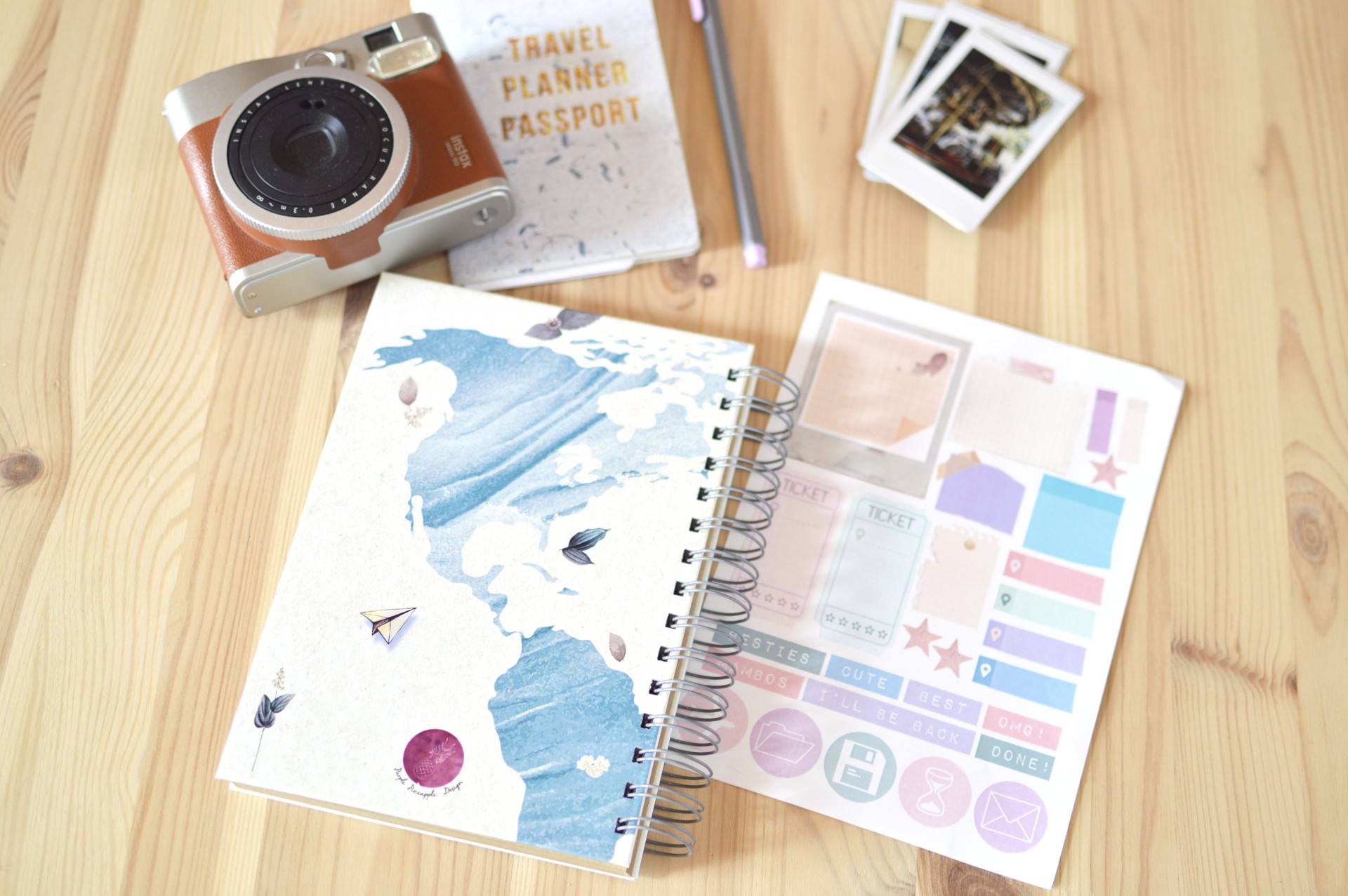 Caderno espiral com capa azul e folhas adesivas coloridas em mesa de madeira com câmera e livro
