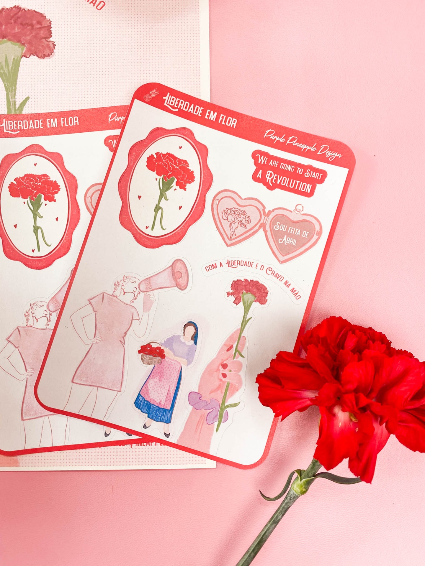 Cartazes ilustrados com flores vermelhas e texto em português e inglês sobre fundo rosa com flor vermelha ao lado