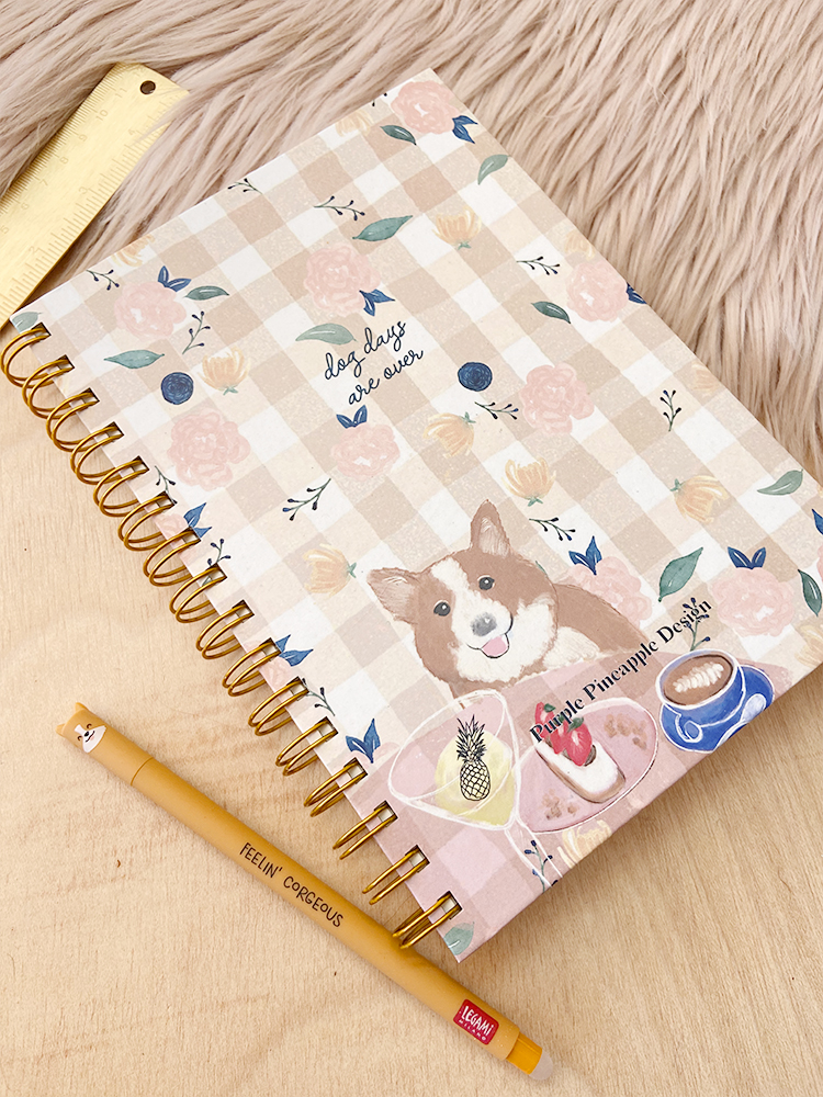 Caderno com capa xadrez bege e branco decorada com flores e cão, espiral dourada, lápis amarelo e tapete bege peludo