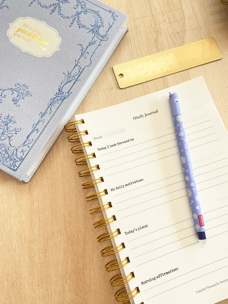 Diário com capa azul, caneta azul clara, régua dourada sobre mesa de madeira