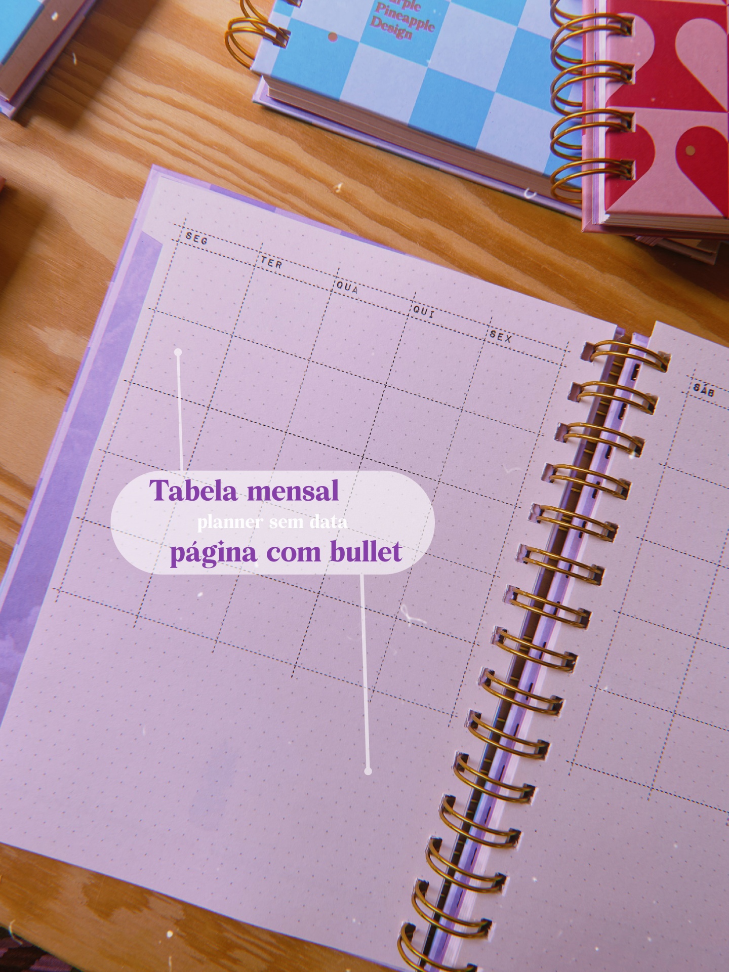 Caderno espiral lilás aberto, página mensal com bullet journal sobre mesa de madeira