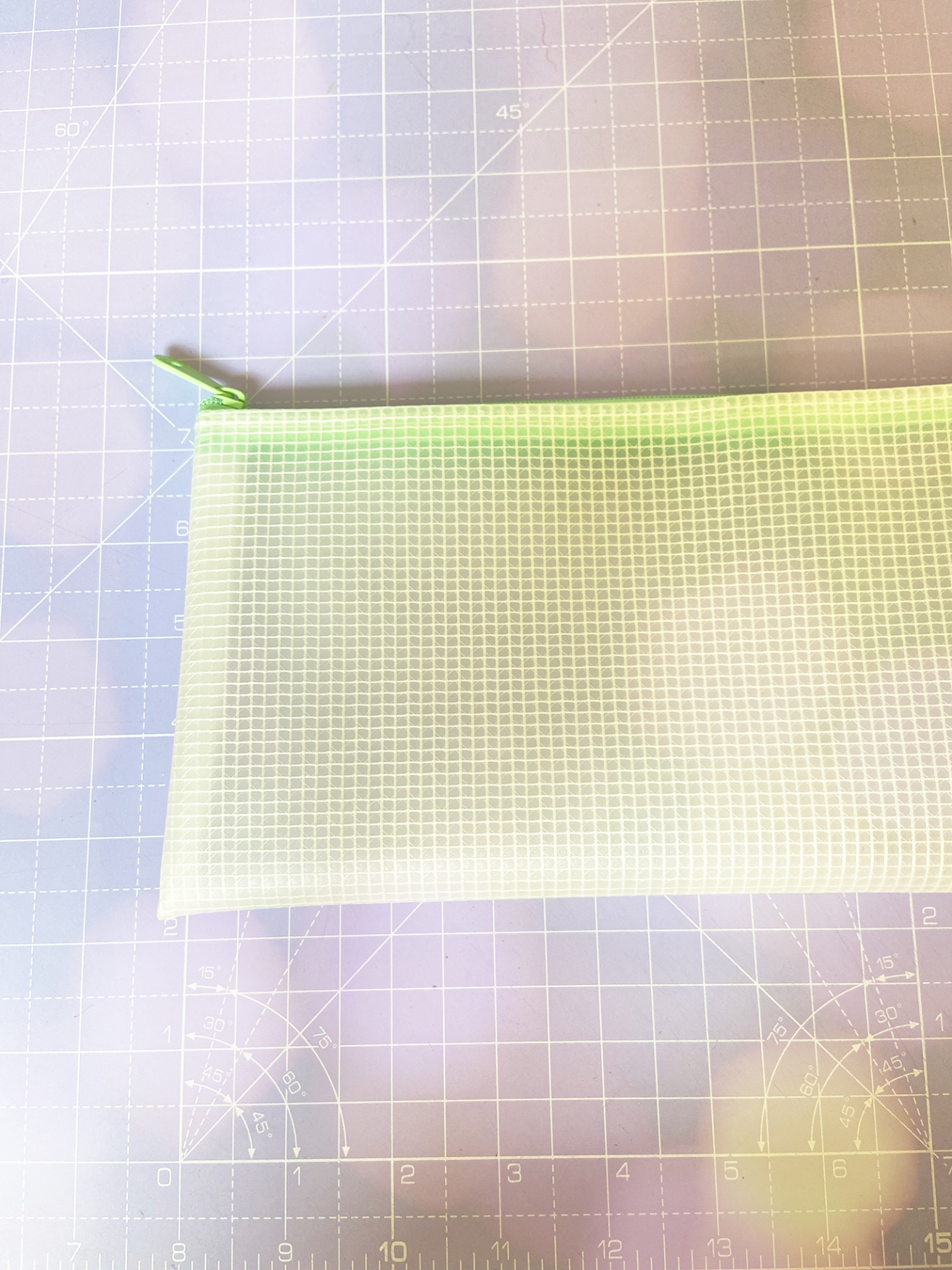 Estojo translúcido branco com fecho zíper verde sobre superfície quadriculada