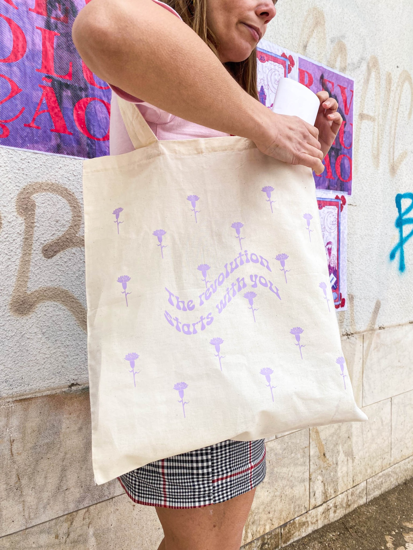 Saco de pano bege com flores lilases e texto 'The revolution starts with you'