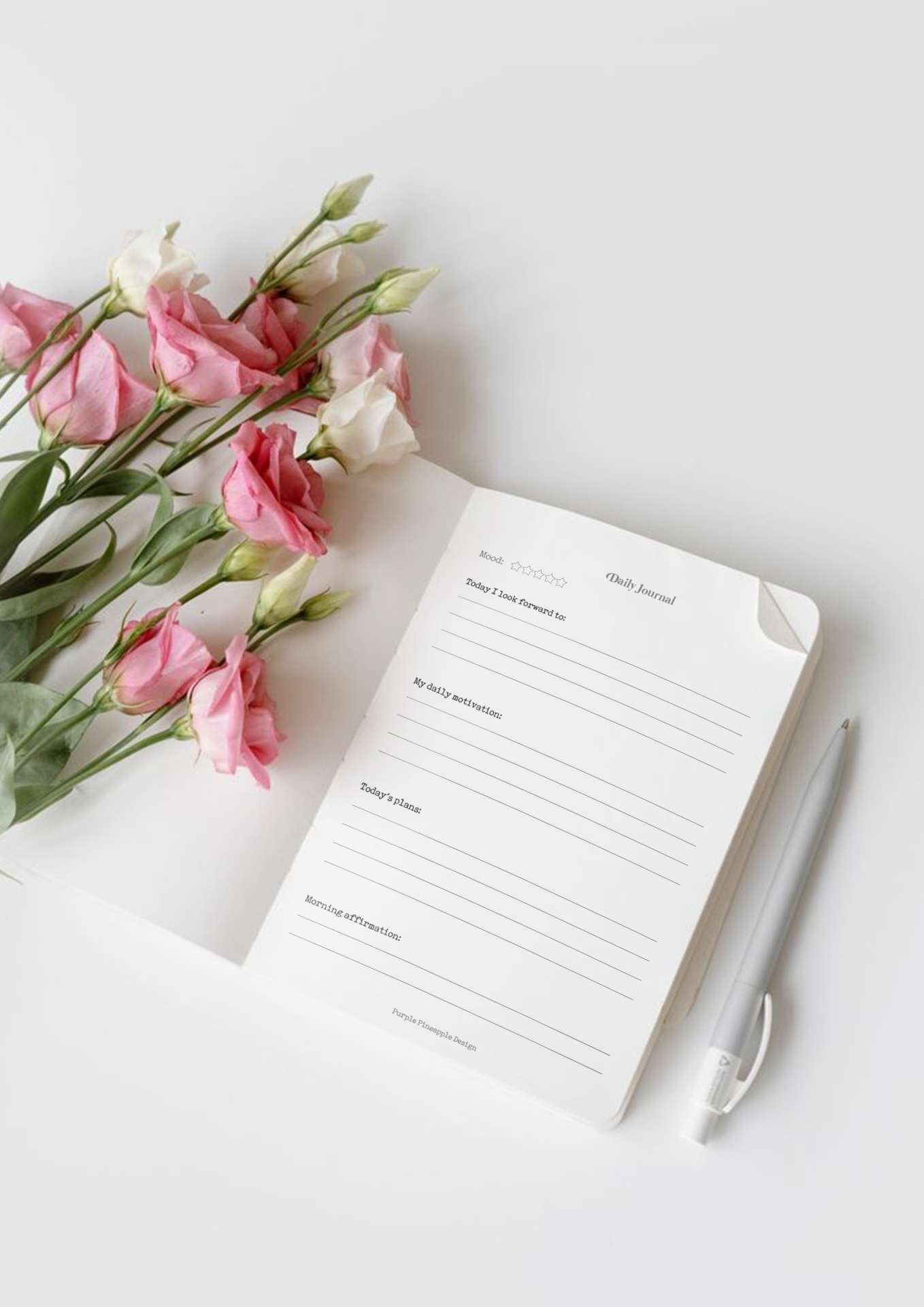 Caderno aberto com texto, caneta branca e ramos de flores rosas e brancas