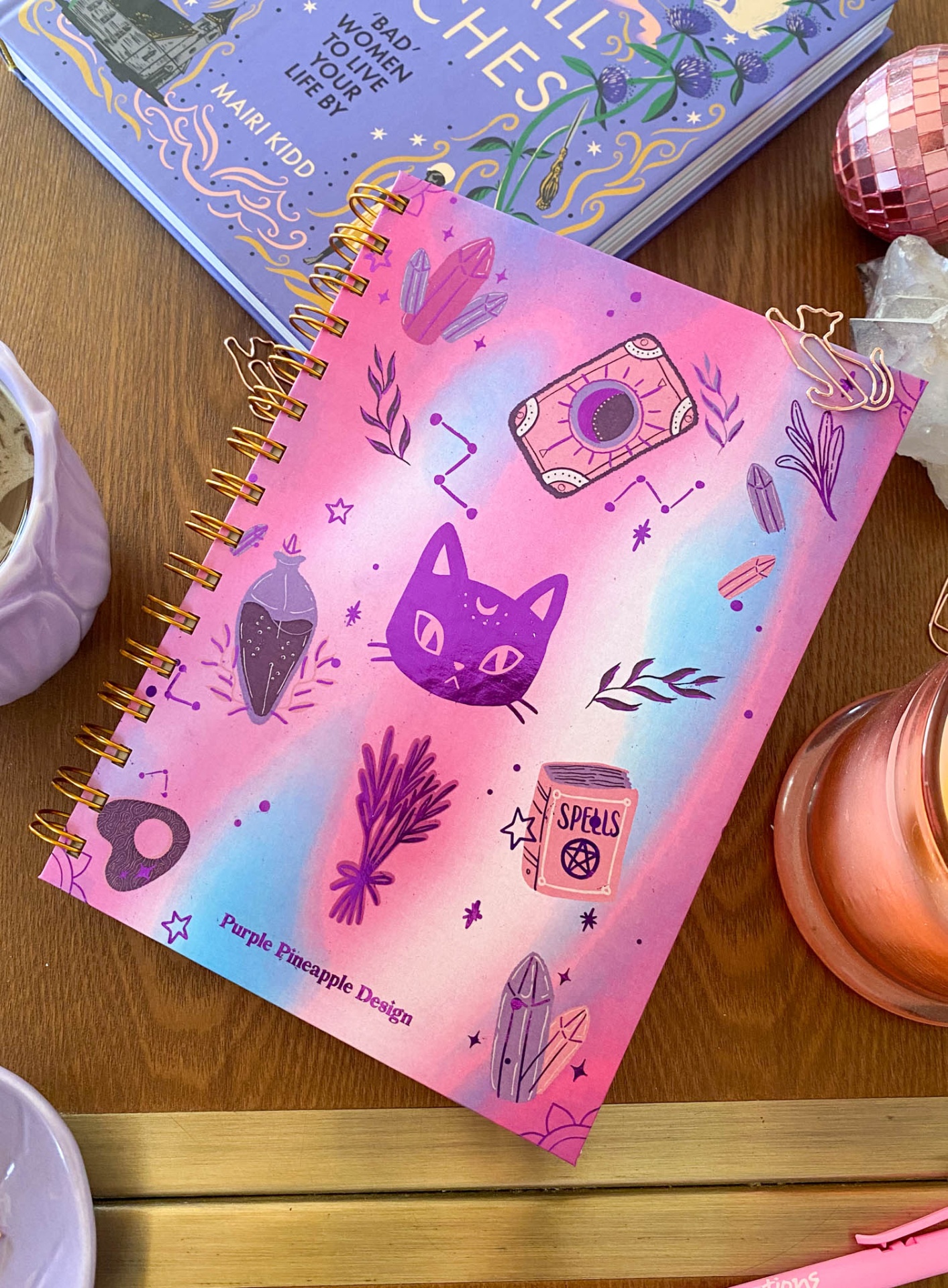 Caderno espiral rosa com ilustrações místicas e texto Purple Pineapple Design