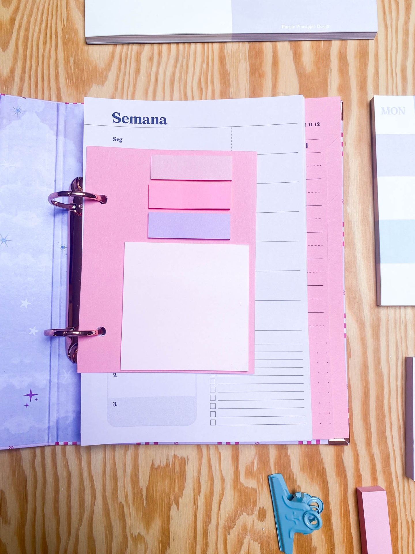 Agenda aberta com post-its rosa e lilás sobre página da semana em português