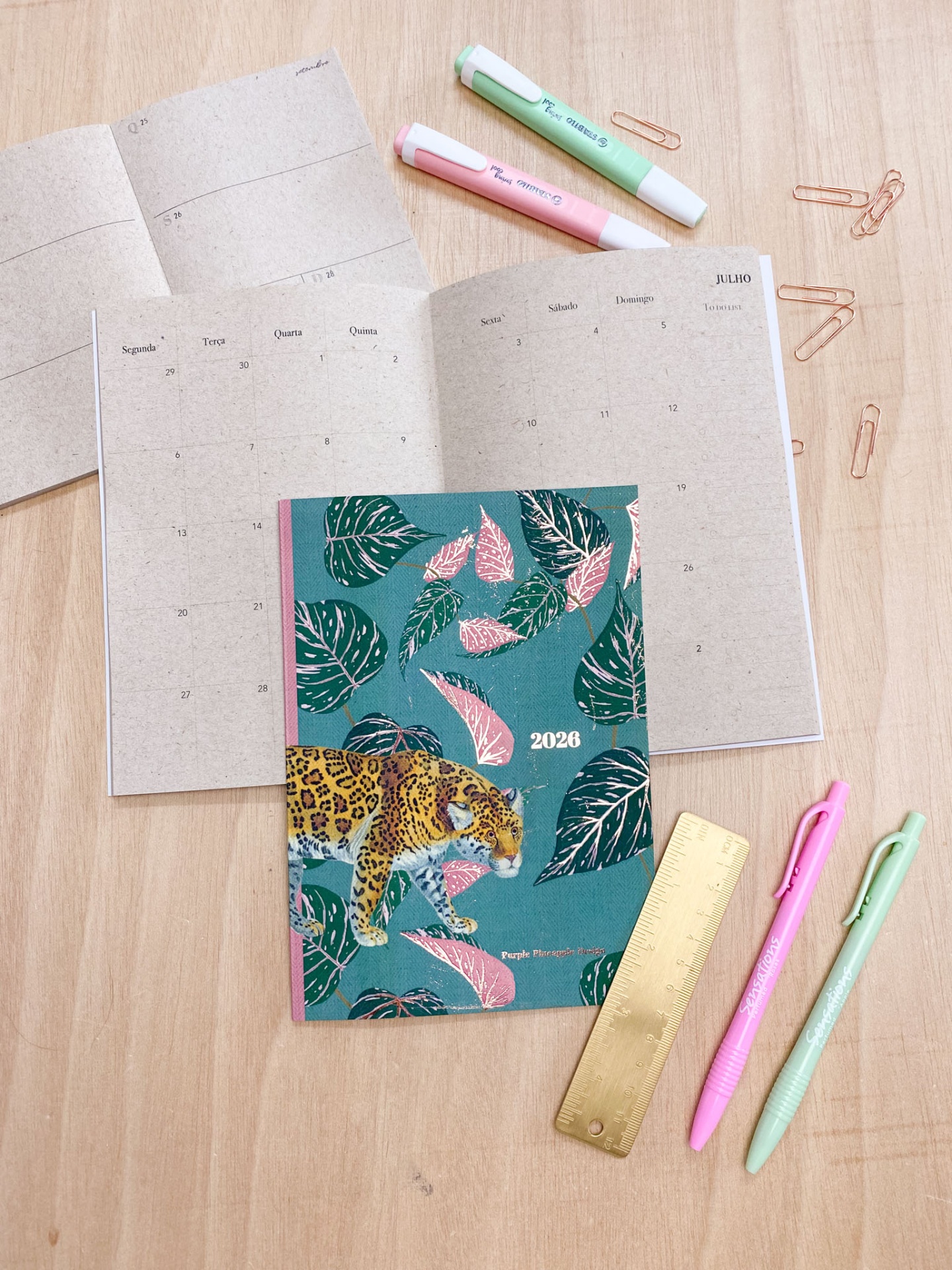 agenda 2026 com capa de onça e folhas, marcadores, canetas, régua dourada e clipes