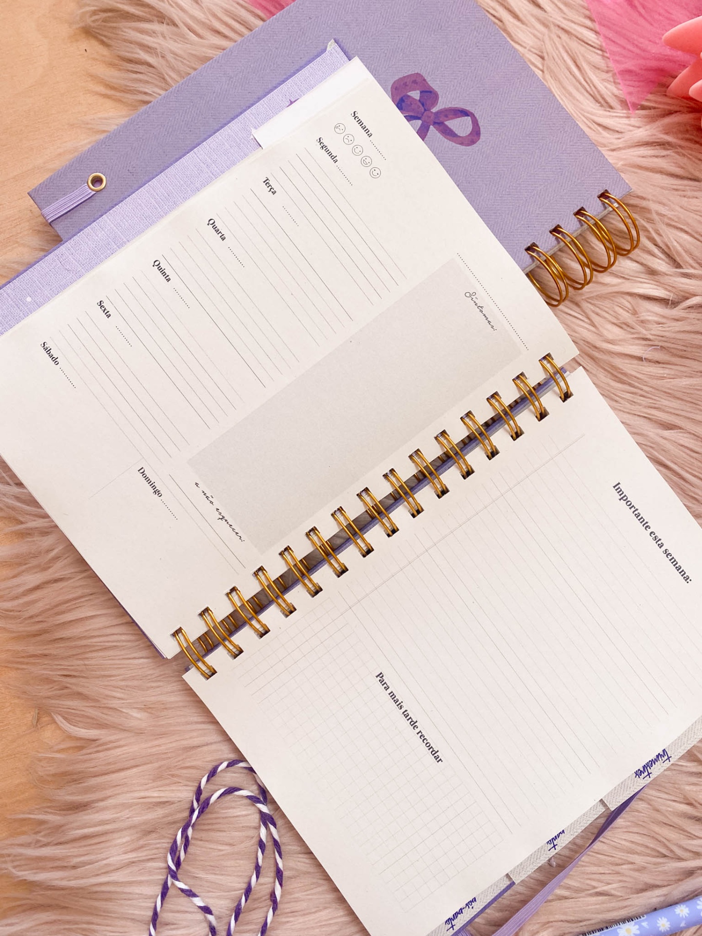 Caderno lilás espiral aberto com páginas para organização semanal sobre tapete rosa