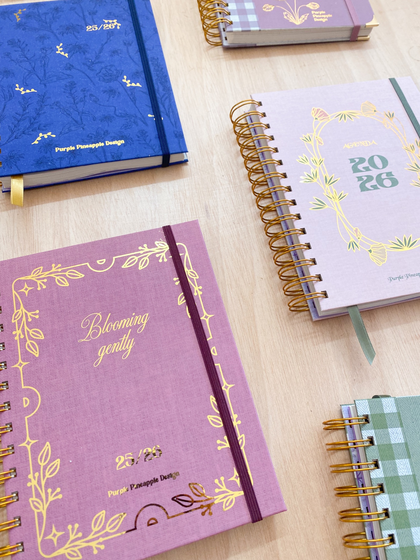 Cadernos e agendas coloridos com capas em tecido e detalhes dourados sobre mesa de madeira