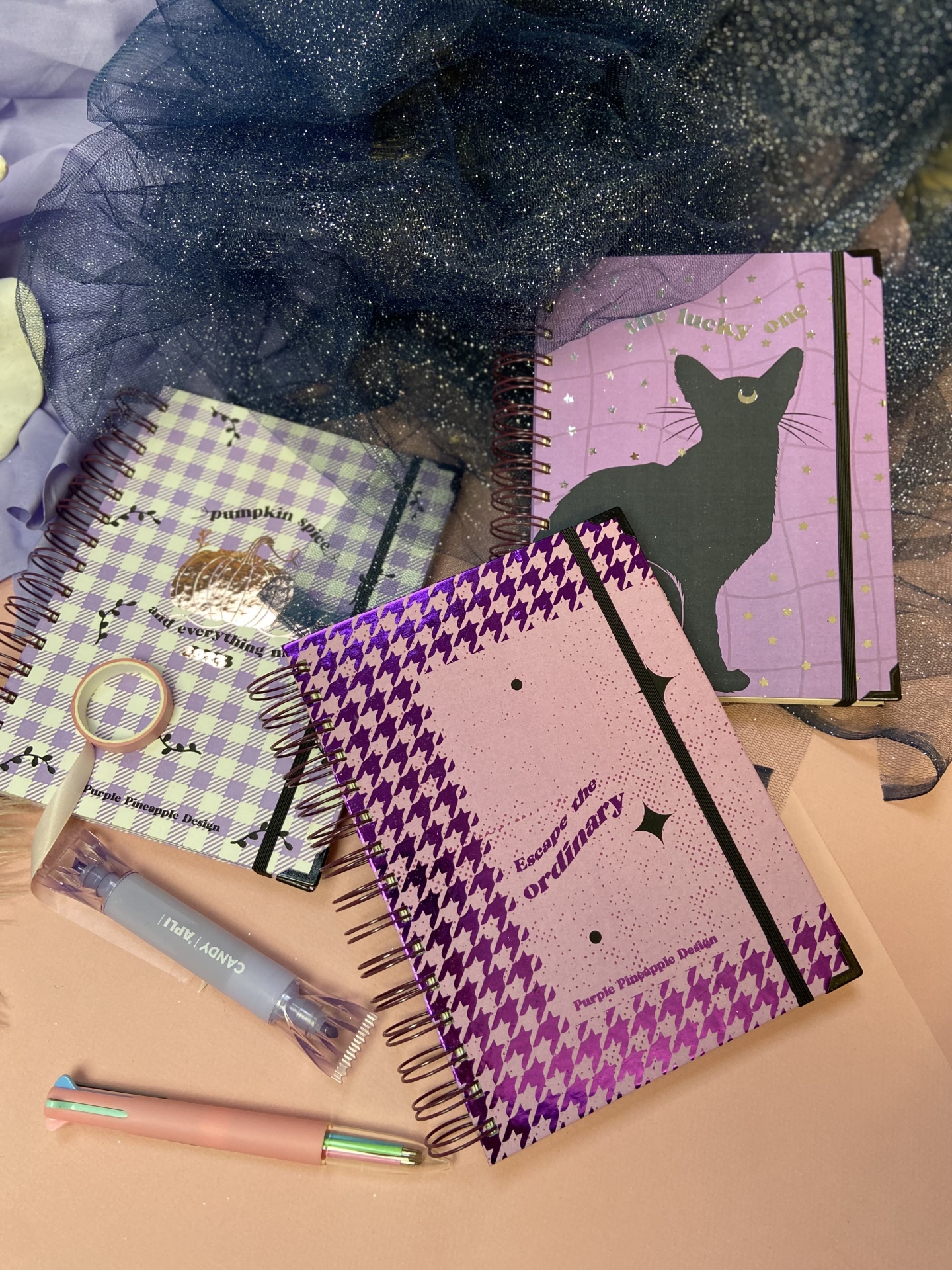 Especial Halloween Três cadernos espiralados com padrões variados, dois pen drives e uma caneta sobre superfície cor de pêssego