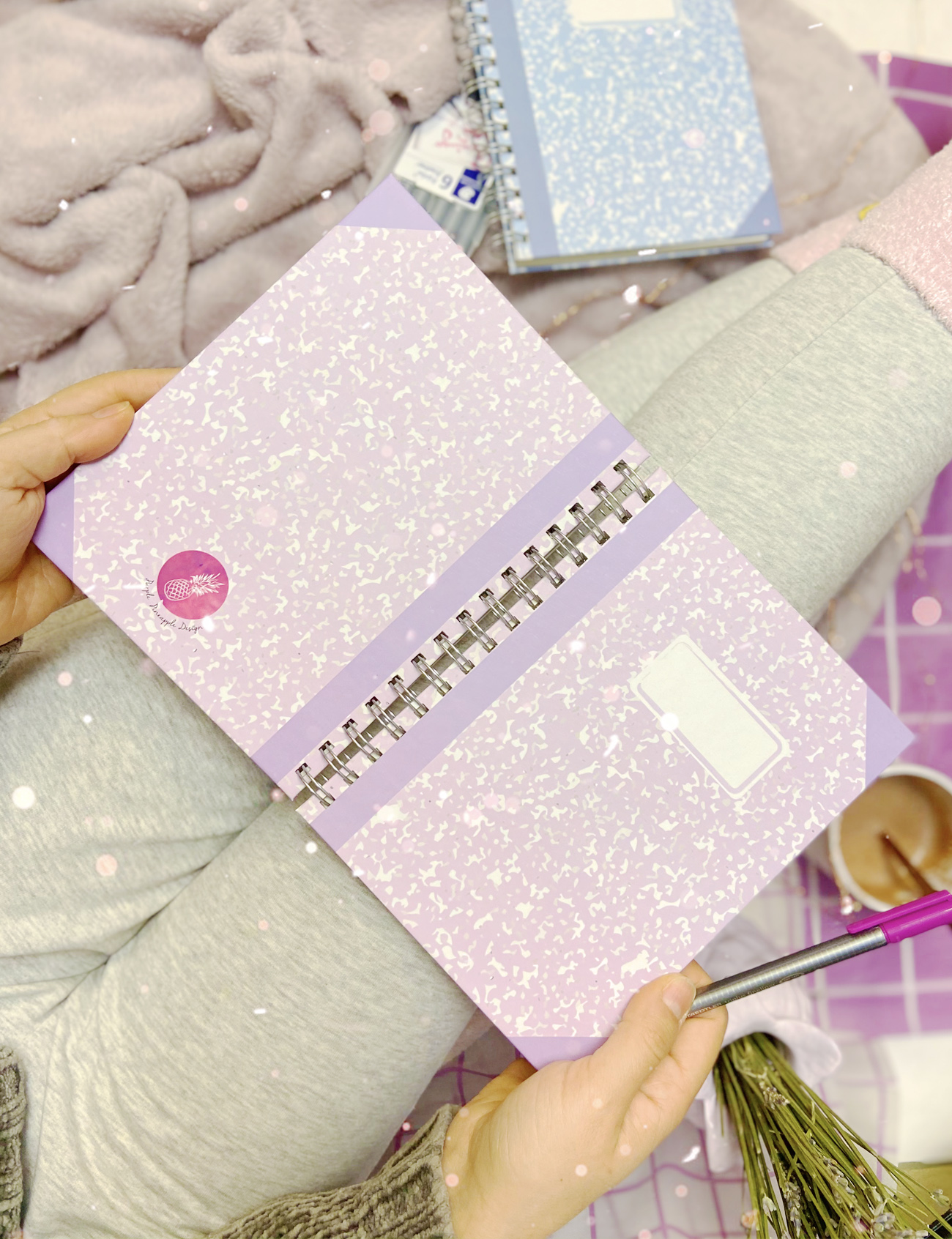 Caderno de padrão rosa claro com argolas e etiqueta branca, mãos segurando e pessoa com roupa cinza claro