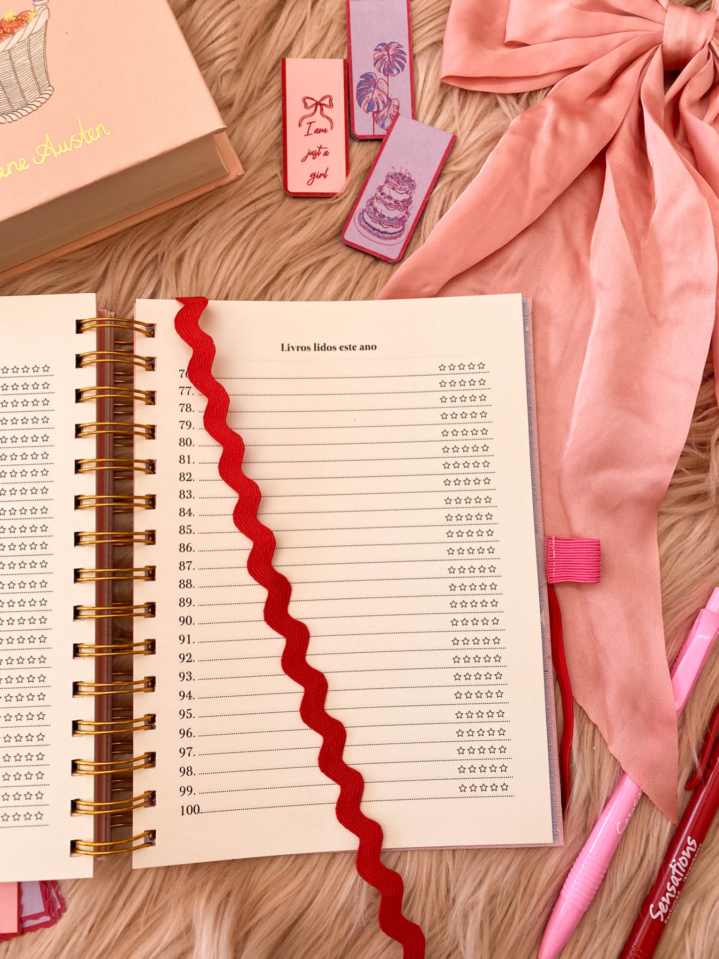 Agenda aberta para livros lidos com marcador vermelho,a caneta Stabilo rosa,e marcadores coloridos sobre fundo felpudo