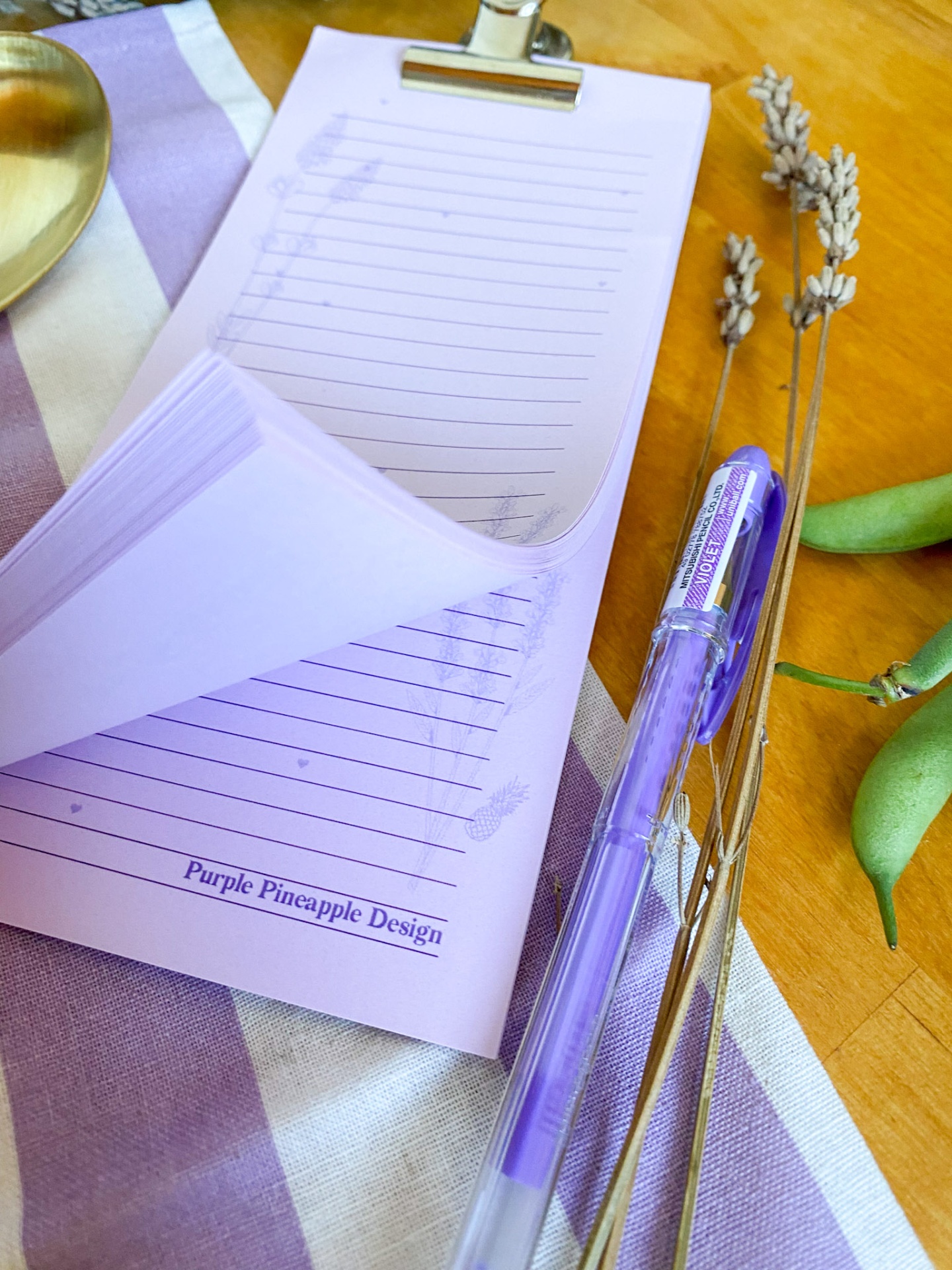 Bloco de notas roxo com caneta roxa e raminhos secos sobre tecido às riscas