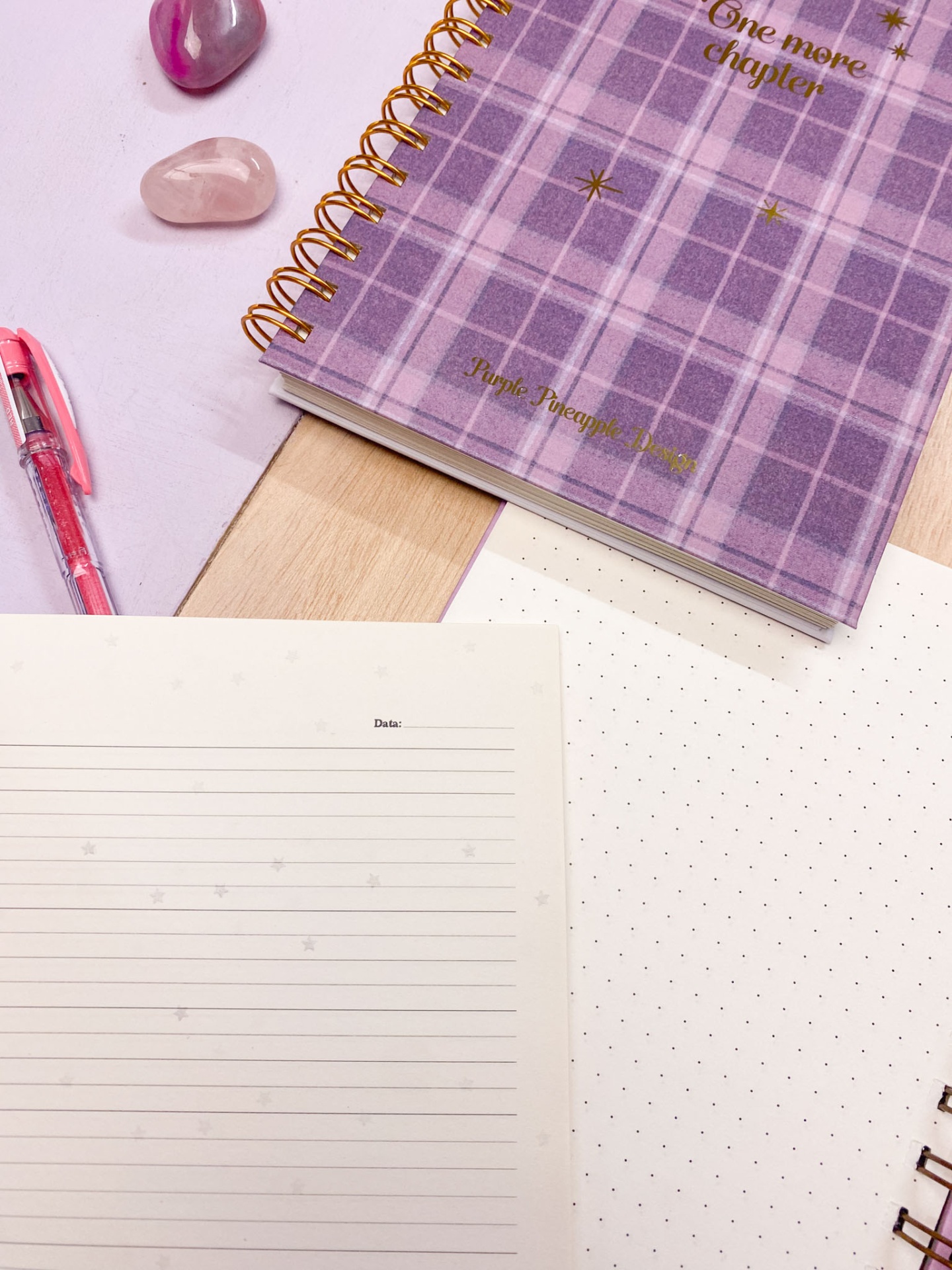 Caderno espiral lilás padrão xadrez com texto dourado e acessórios sobre mesa