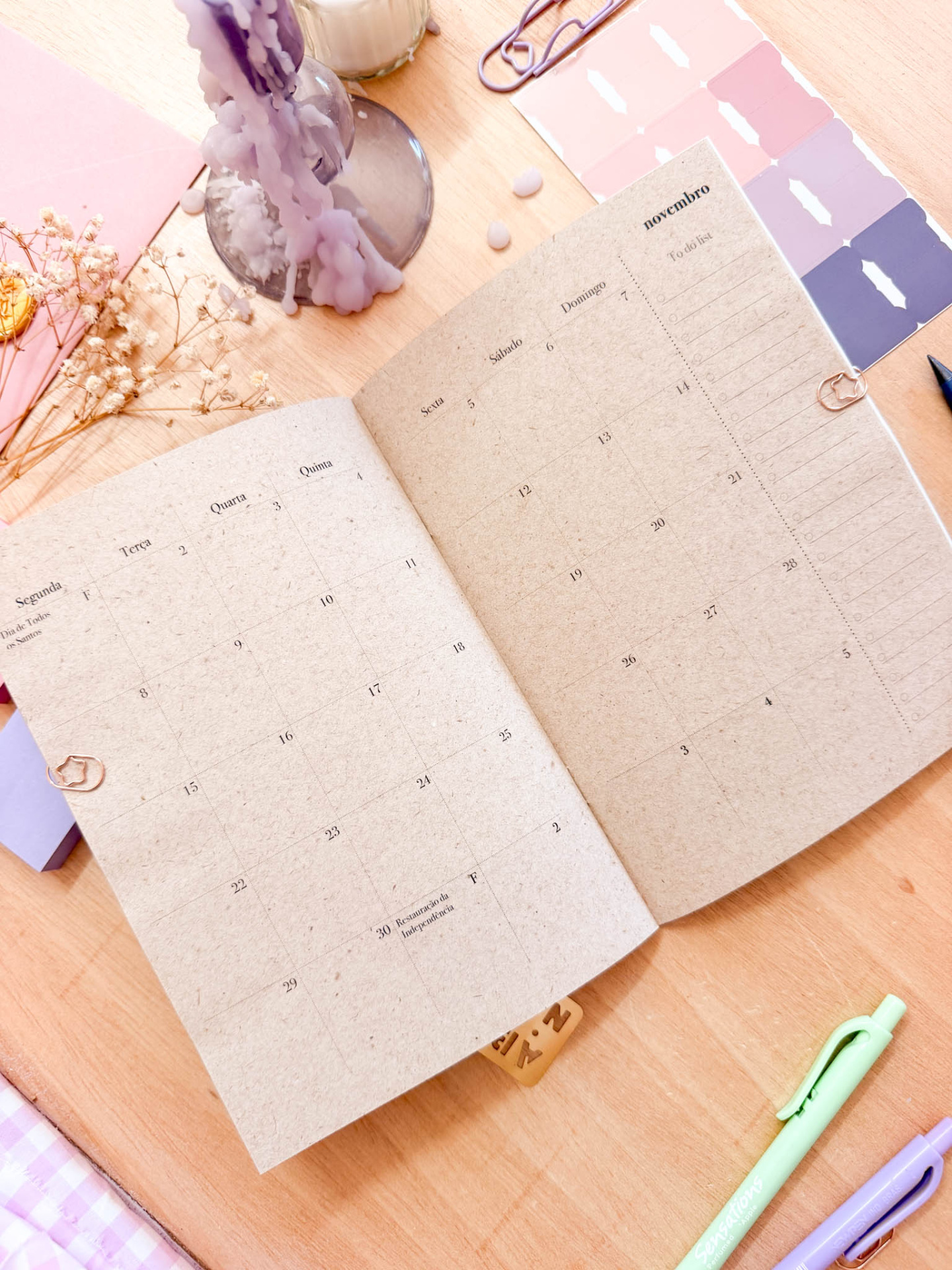 Agenda diária aberta com decoração e artigos de papelaria sobre mesa de madeira.
