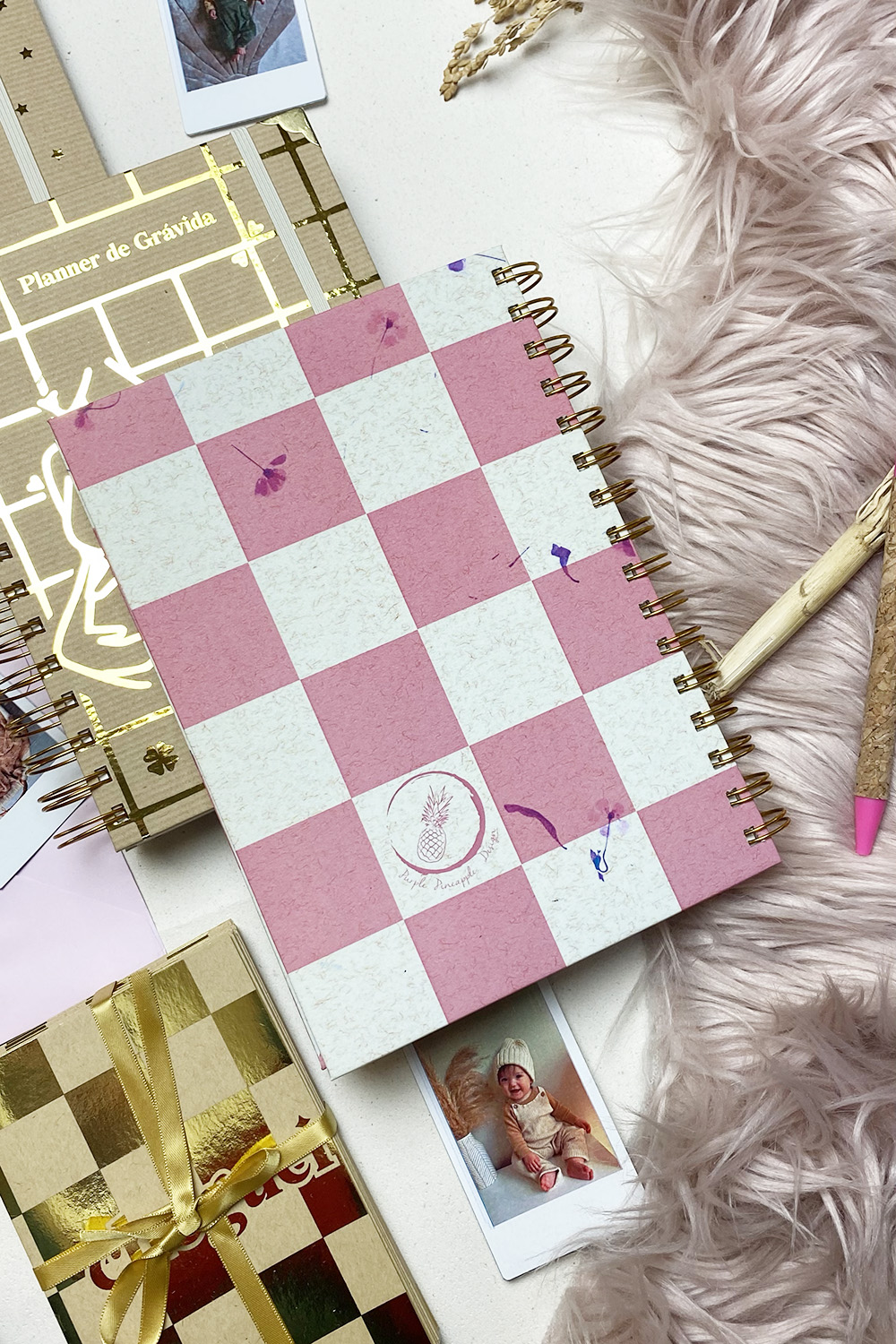 Caderno espiral quadriculado com texto 'Planner de Grávida' e canetas sobre tecido felpudo rosa