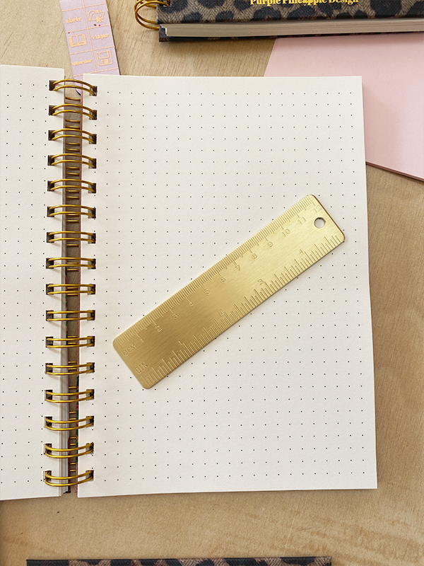 Caderno com folhas pontilhadas e régua metálica dourada sobre ele