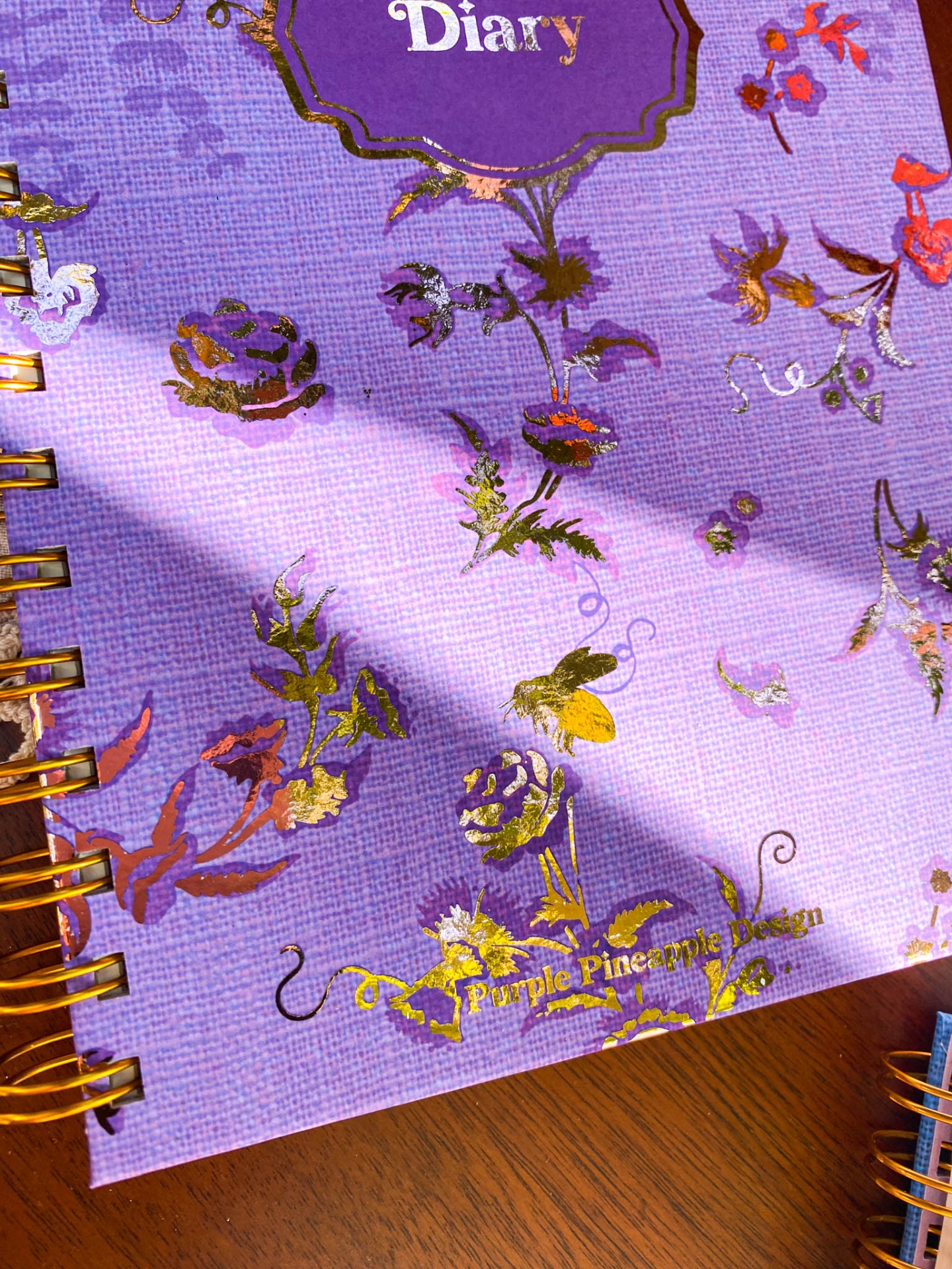 Caderno diário roxo com flores douradas e encadernação espiral dourada