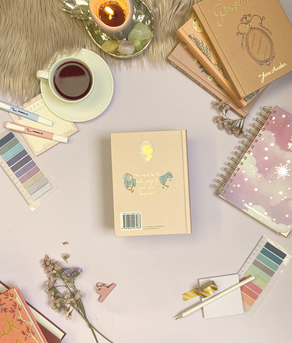 Artigos de papelaria, flores secas, vela acesa e chá sobre mesa clara