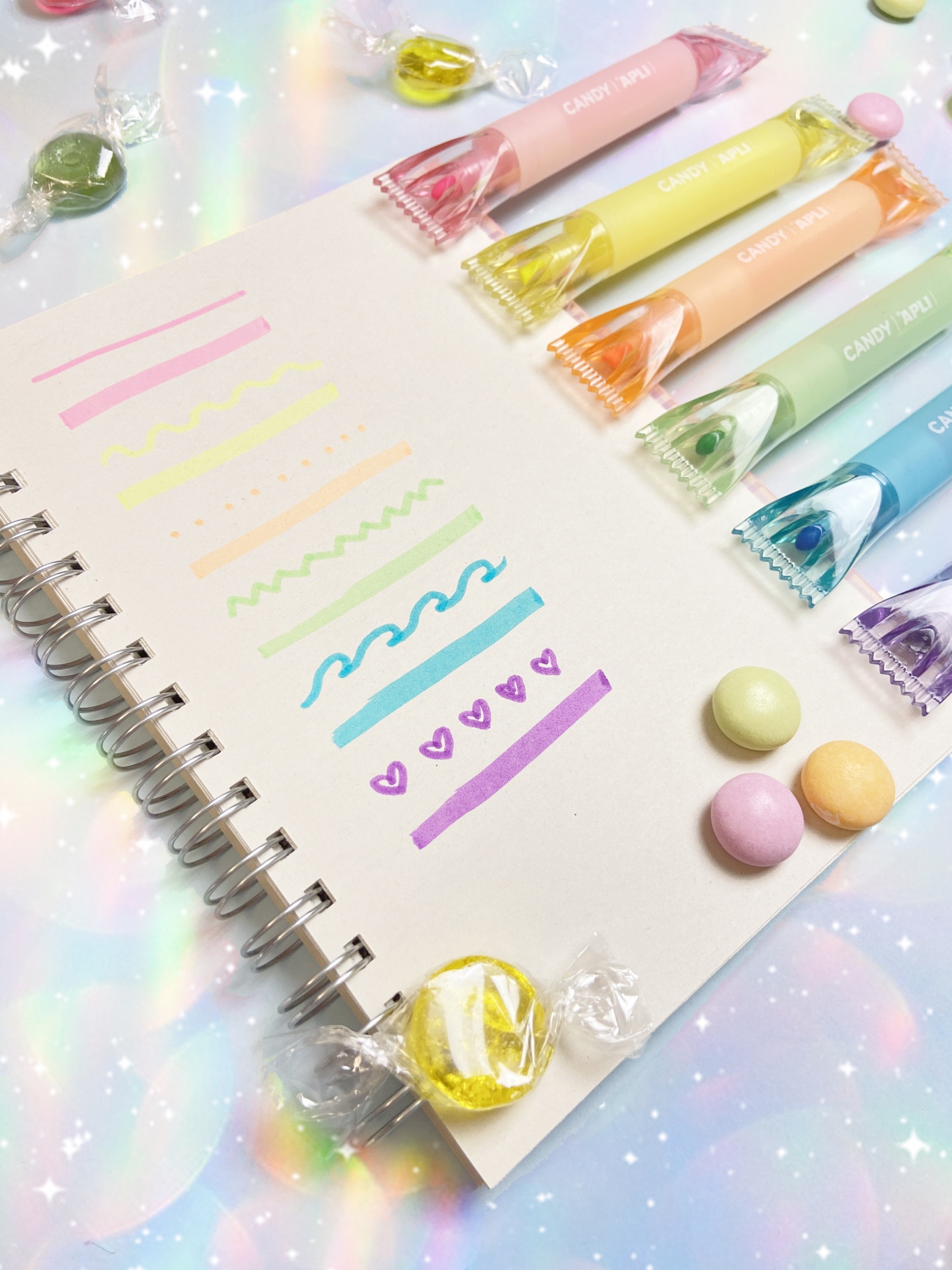 Canetas coloridas Candy Roll dispostas com traços coloridos num caderno aberto
