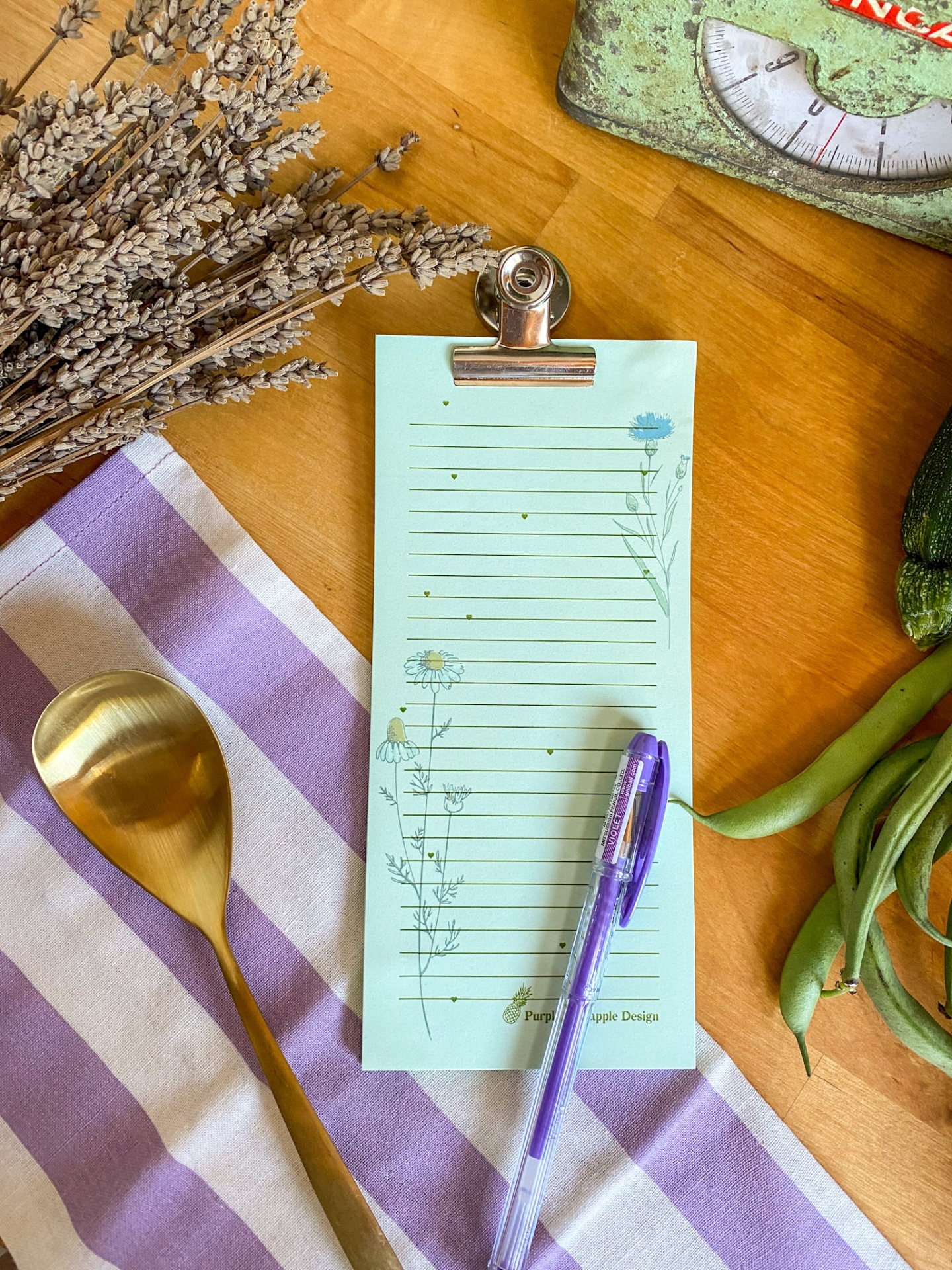 Lista de notas floral presa por clip sobre mesa com utensílios e legumes