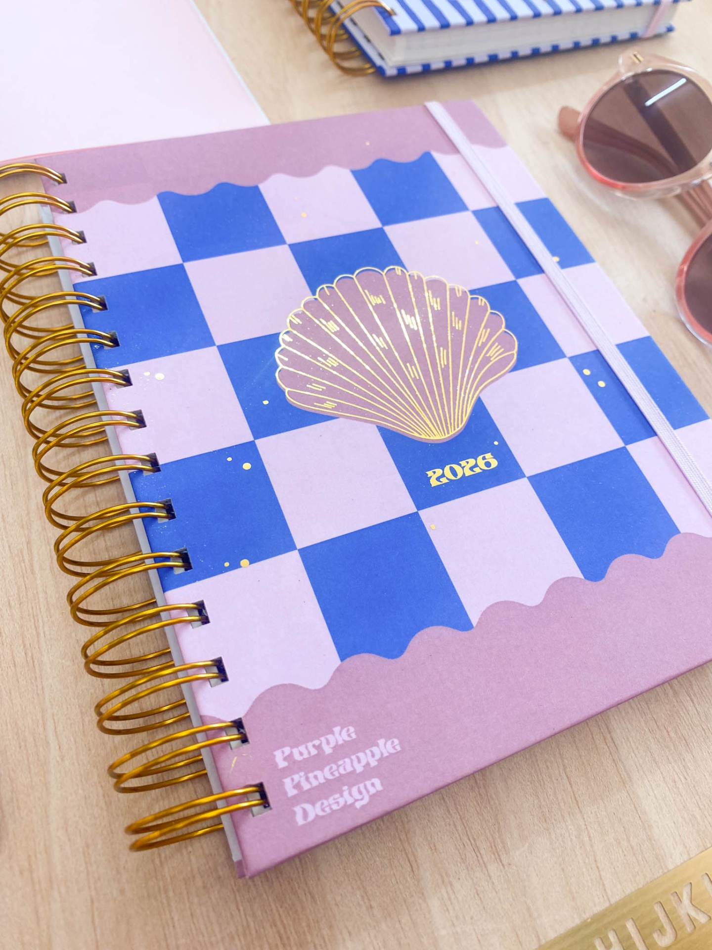 Agenda 2026 com capa xadrez azul e lilás com concha dourada e espiral dourada