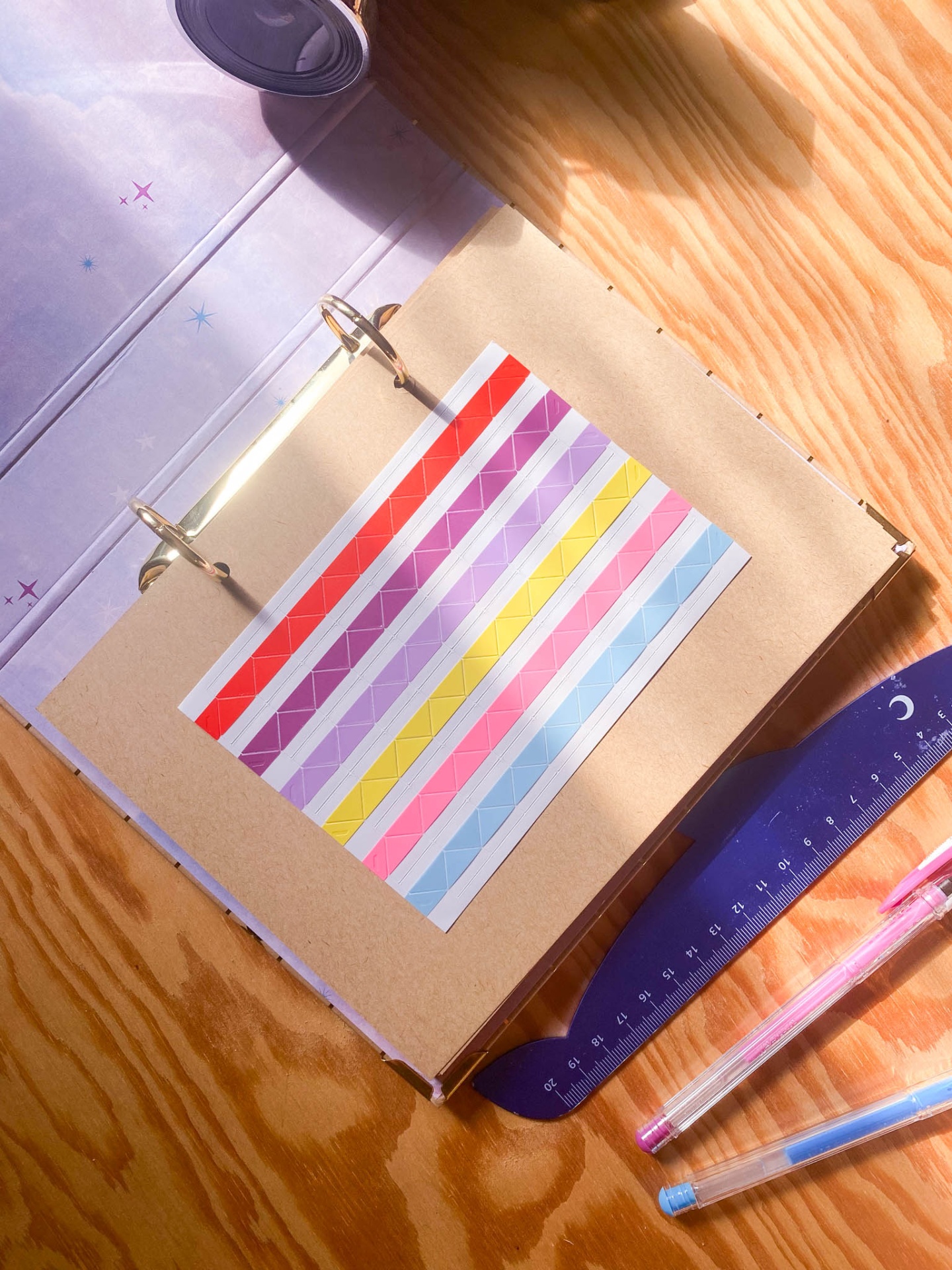 Caderno de argolas com tiras adesivas coloridas numa mesa de madeira com régua e canetas