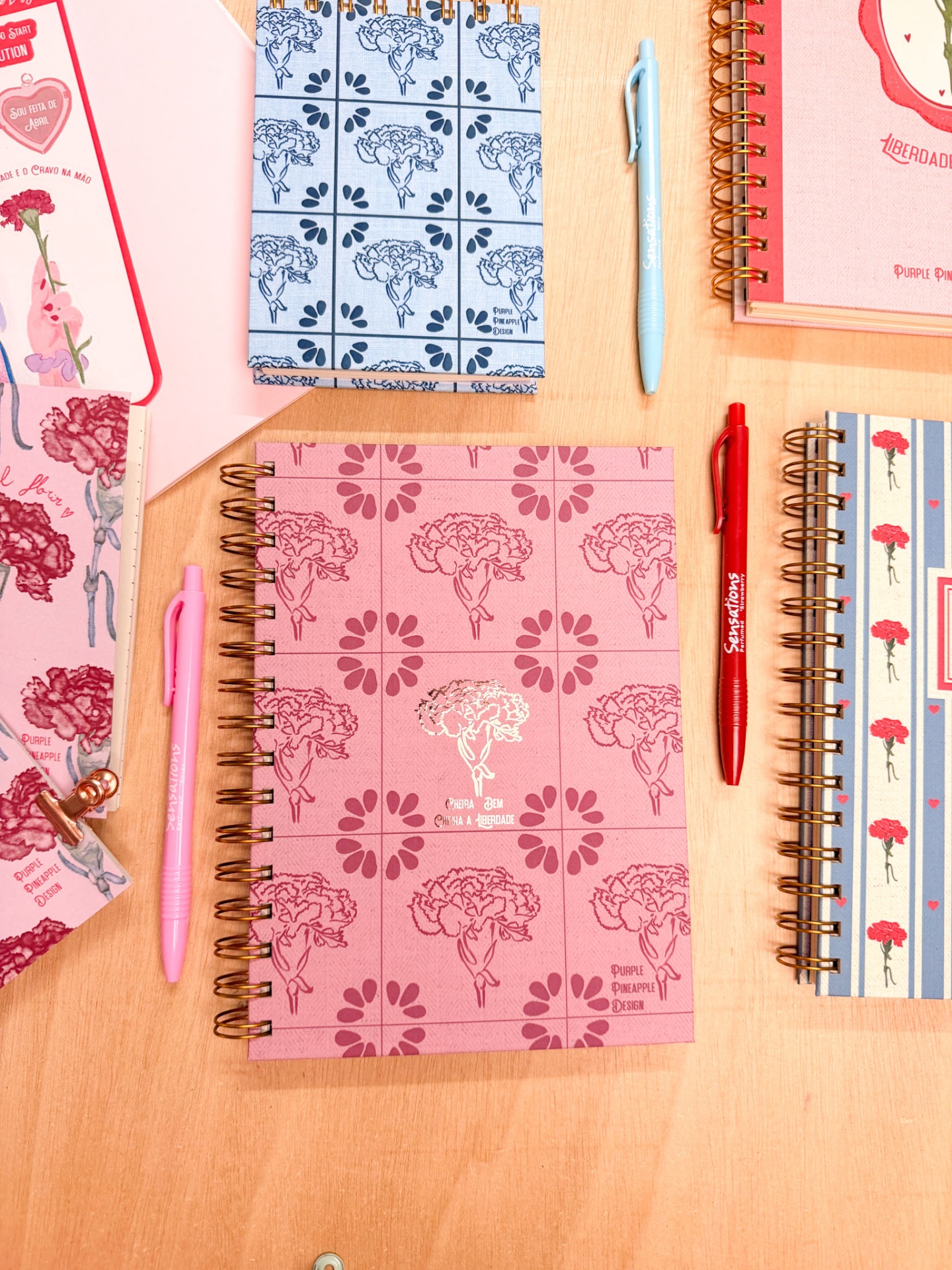 Cadernos espiral com capas florais e canetas coloridas sobre mesa de madeira