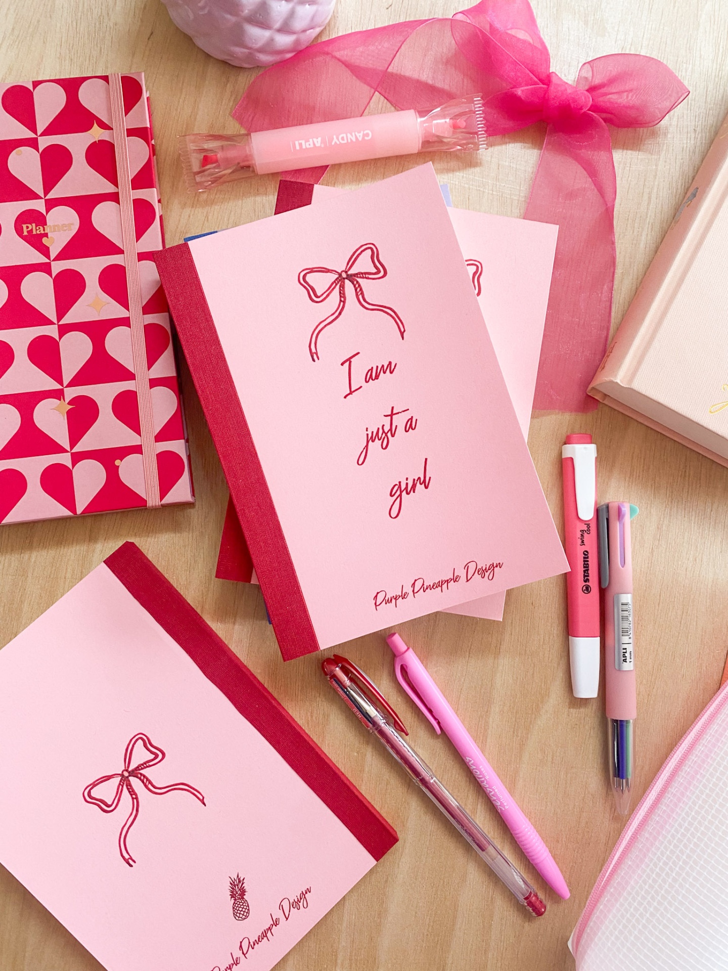 Material de escritório e papelaria rosa com cadernos, canetas e estojo em fundo de madeira.