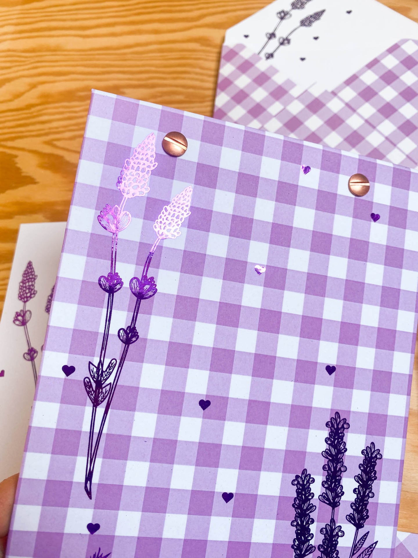 Caderno xadrez lilás e branco com desenhos de flores roxas e corações, com ilhós de metal cobre