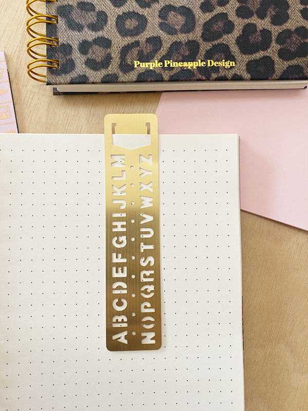 Marcador de livro dourado com letras do alfabeto e agenda com padrão animal print