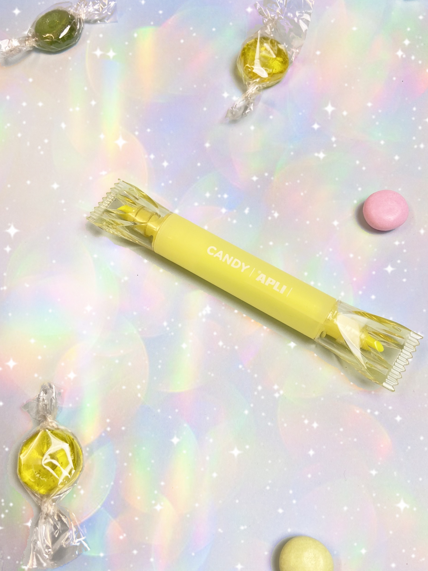 Pacote amarelo de doce com texto e vários doces coloridos embrulhados num fundo brilhante e translúcido.