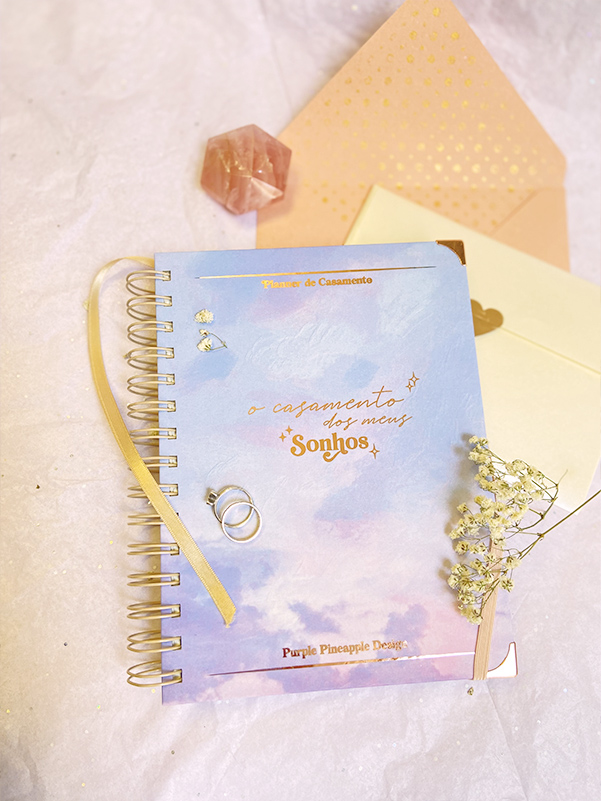 Caderno azul e rosa com texto dourado e acessórios de casamento sobre fundo branco