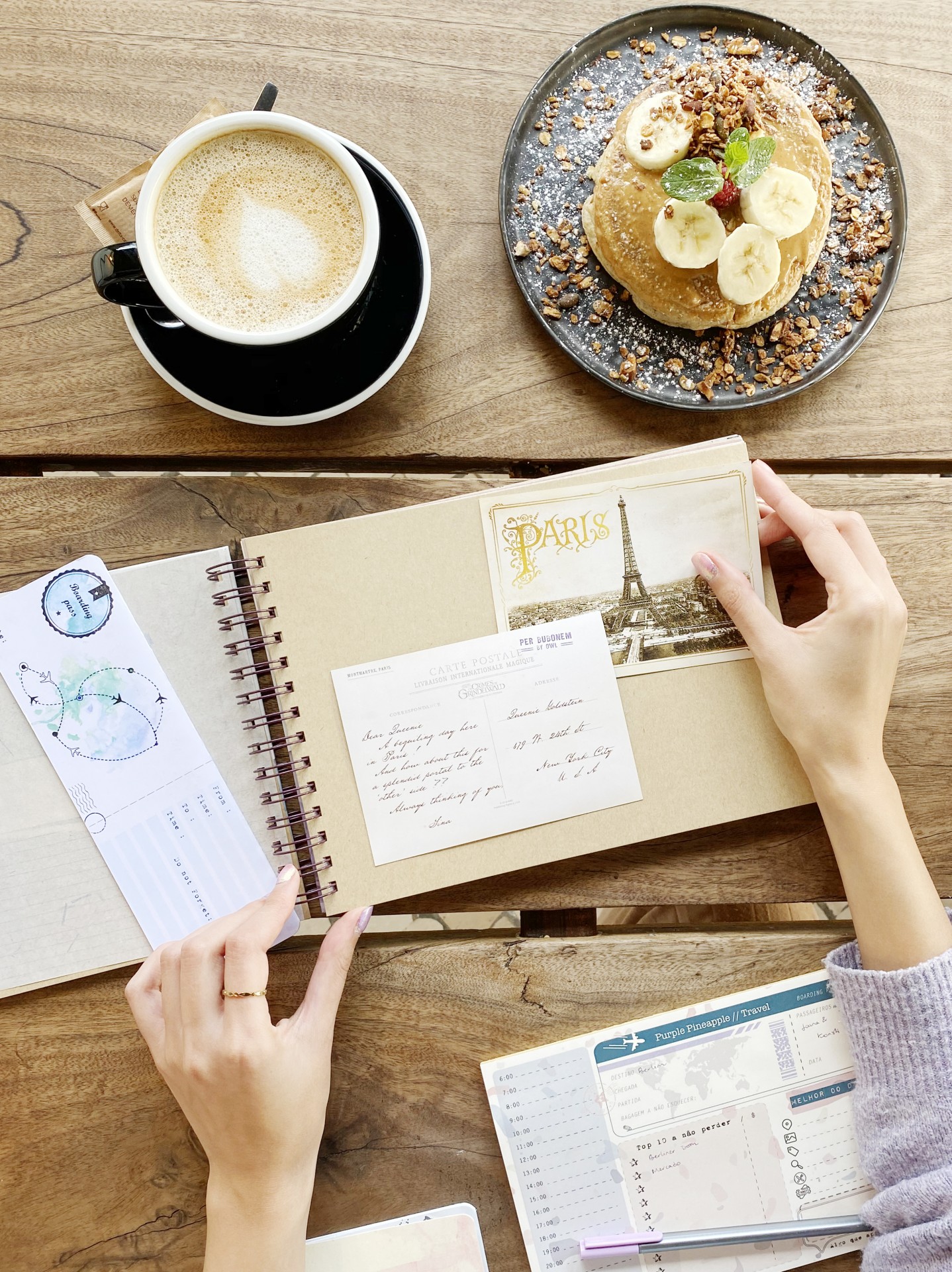 Cappuccino, panquecas com banana e nozes e caderno de viagem sobre mesa de madeira clara