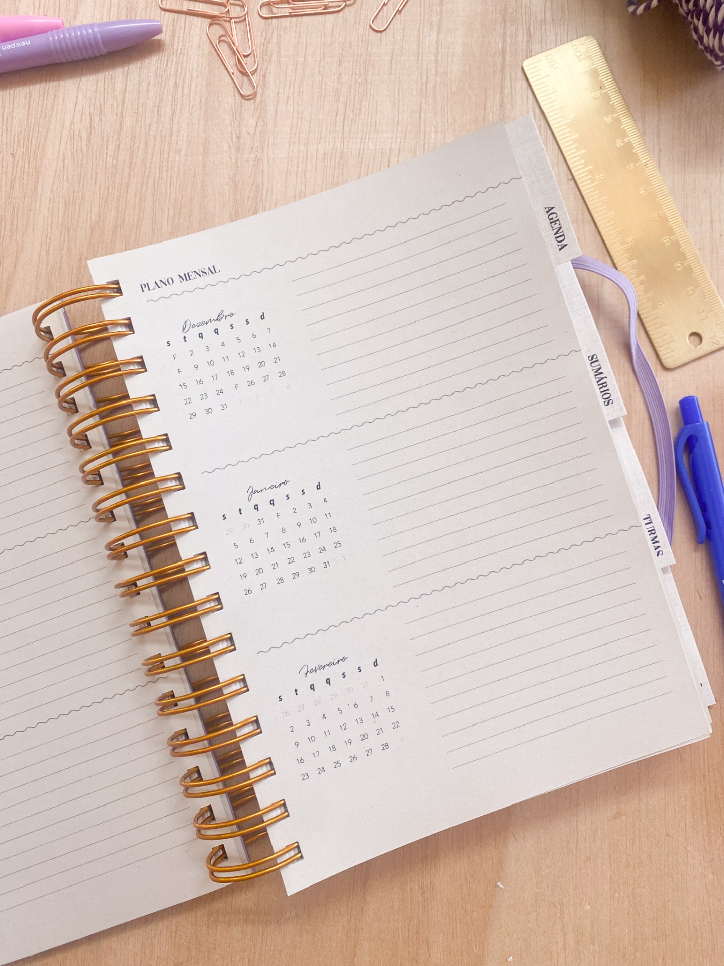 Agenda mensal com calendário e divisórias sobre mesa de madeira com material de escritório