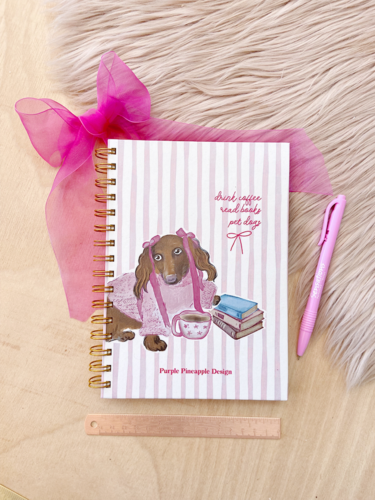 Caderno decorado com cão e livros, caneta rosa e régua