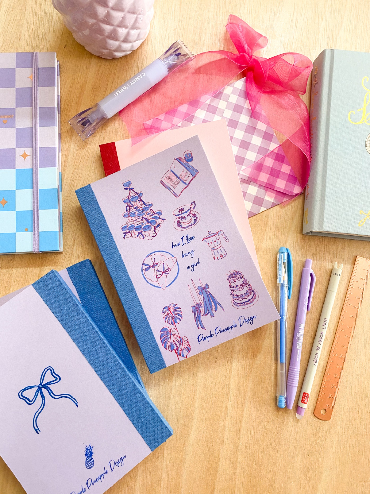 Cadernos e canetas coloridas dispostos sobre mesa de madeira com saco rosa e régua