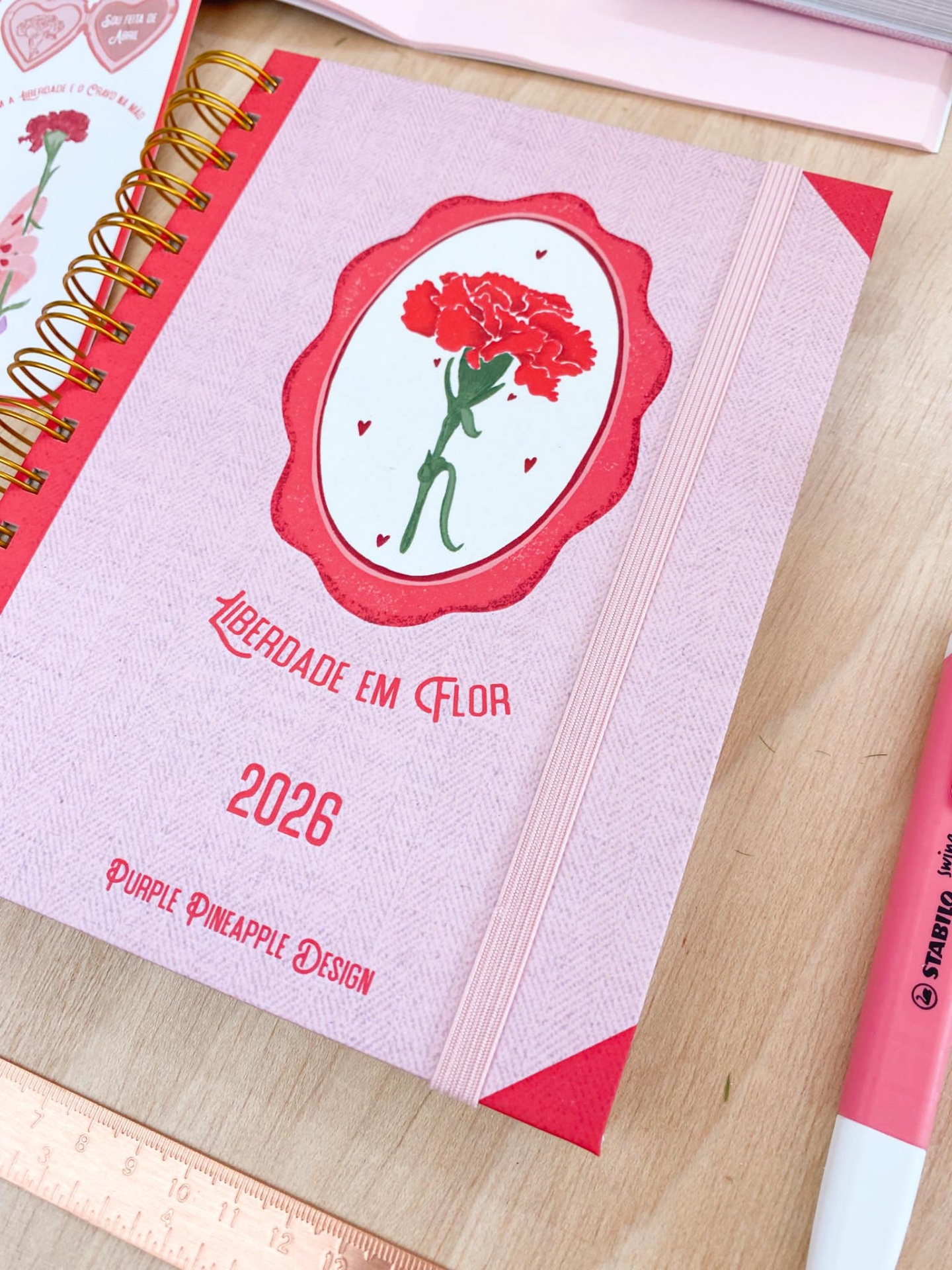 Agenda 2026 rosa claro com detalhes vermelhos e flor vermelha na capa