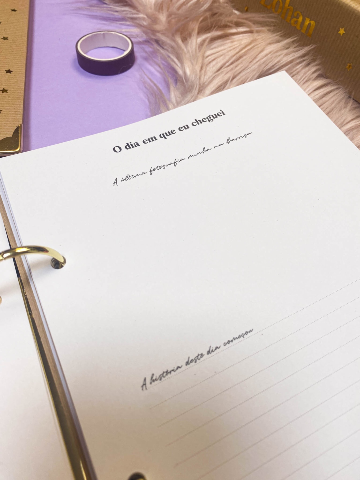 Folha de caderno branca com texto em português, argolas metálicas, sobre superfície lilás com objeto redondo e tecido peludo