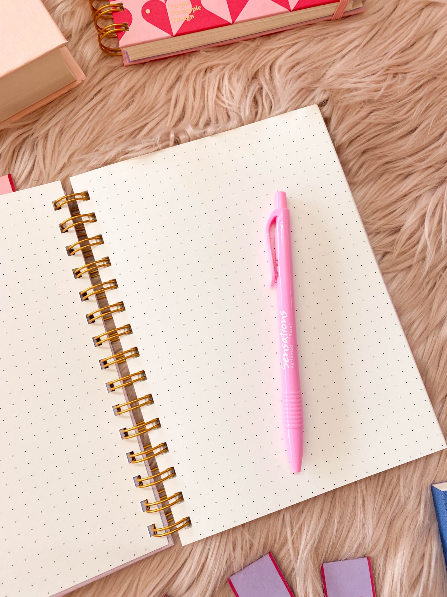 Caderno aberto com páginas pontilhadas e caneta rosa sobre tecido felpudo