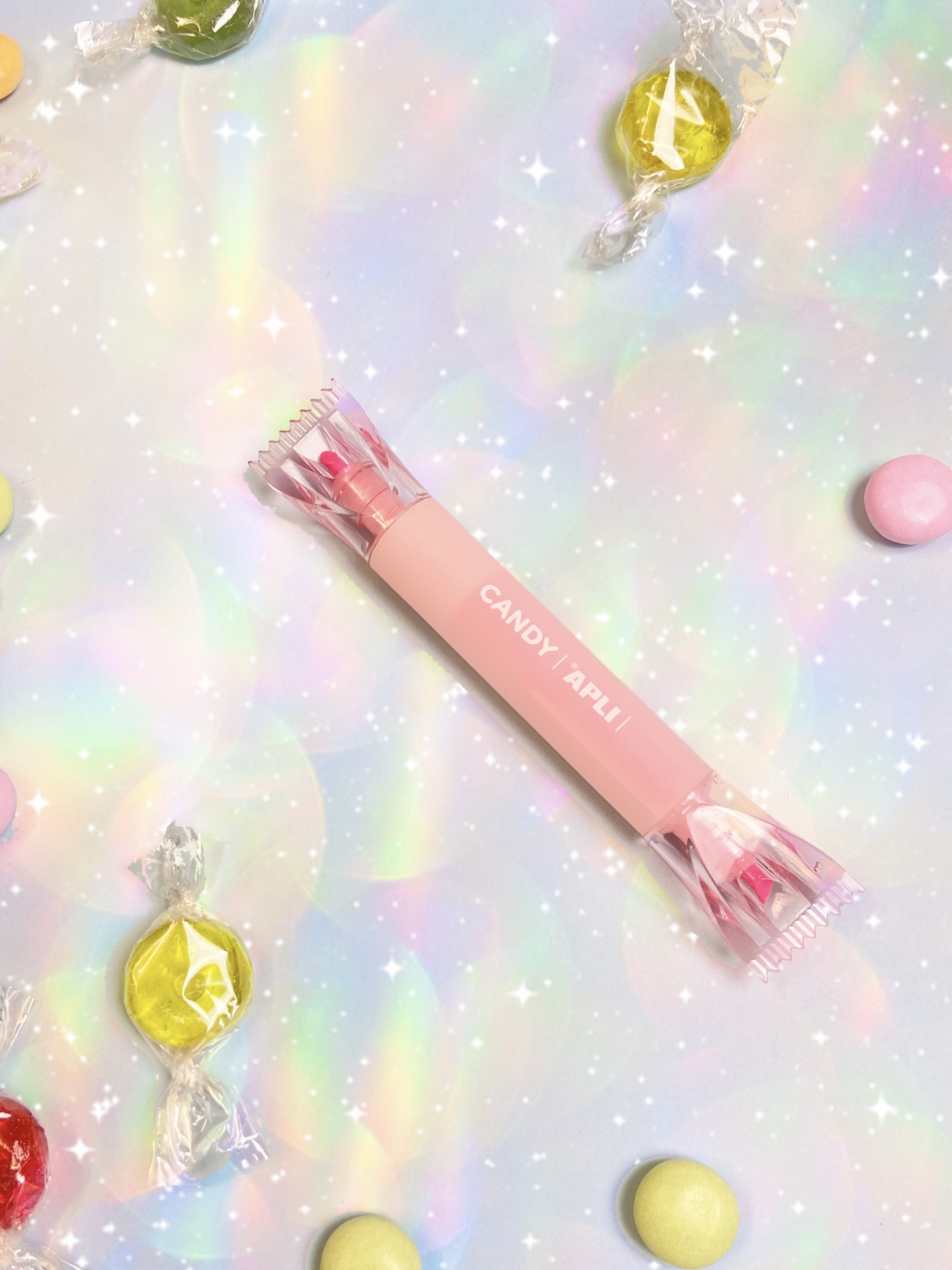 Doce em embalagem rosa e vários doces coloridos sobre superfície brilhante