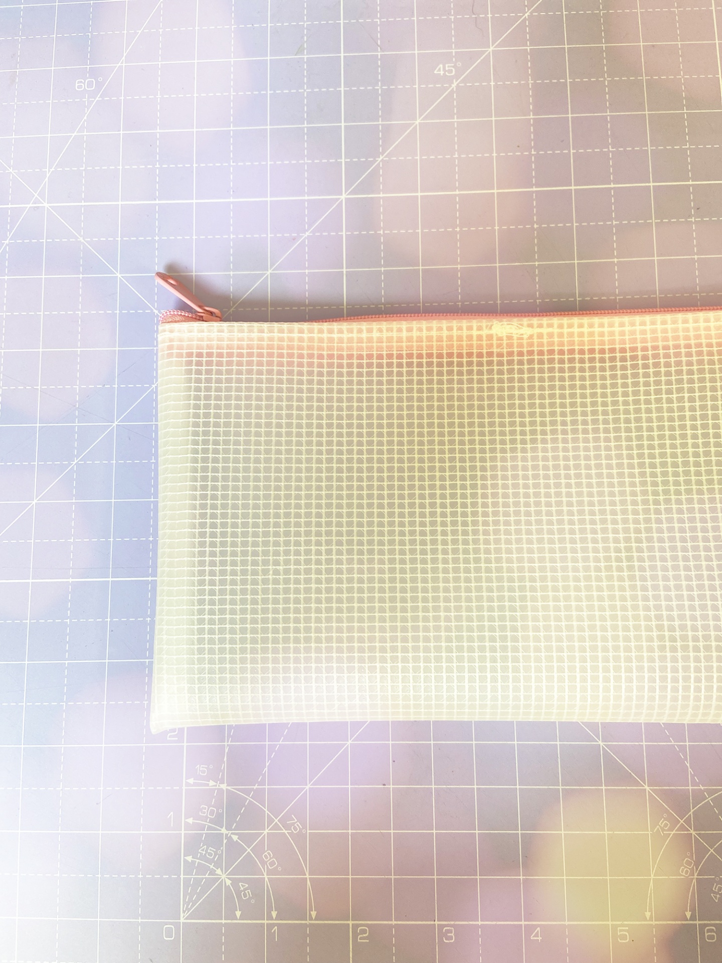 Estojo translúcido com padrão quadriculado e fecho zíper rosa sobre superfície com linhas de medição