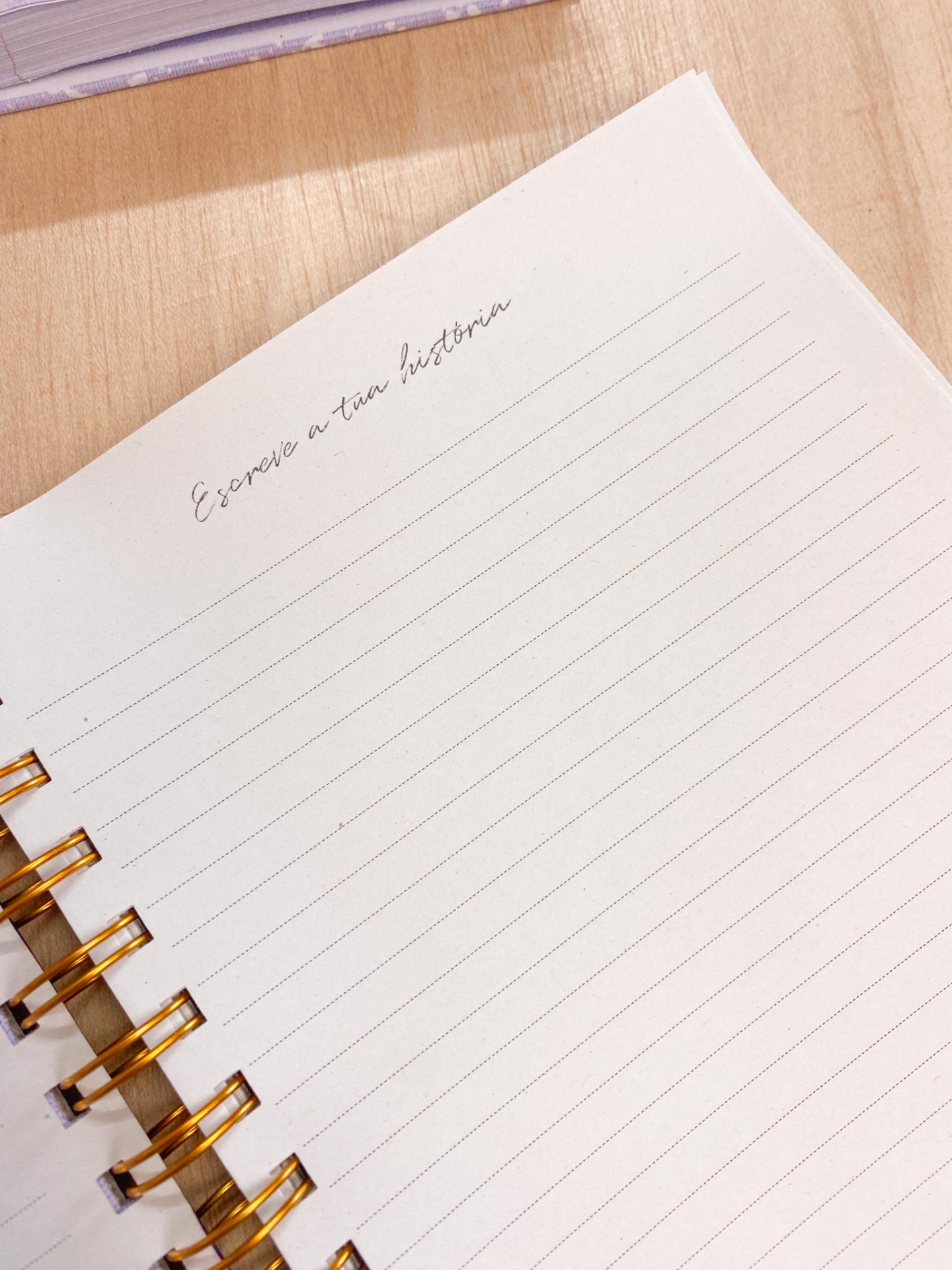 Caderno espiral branco com texto Escreve a tua história numa mesa de madeira