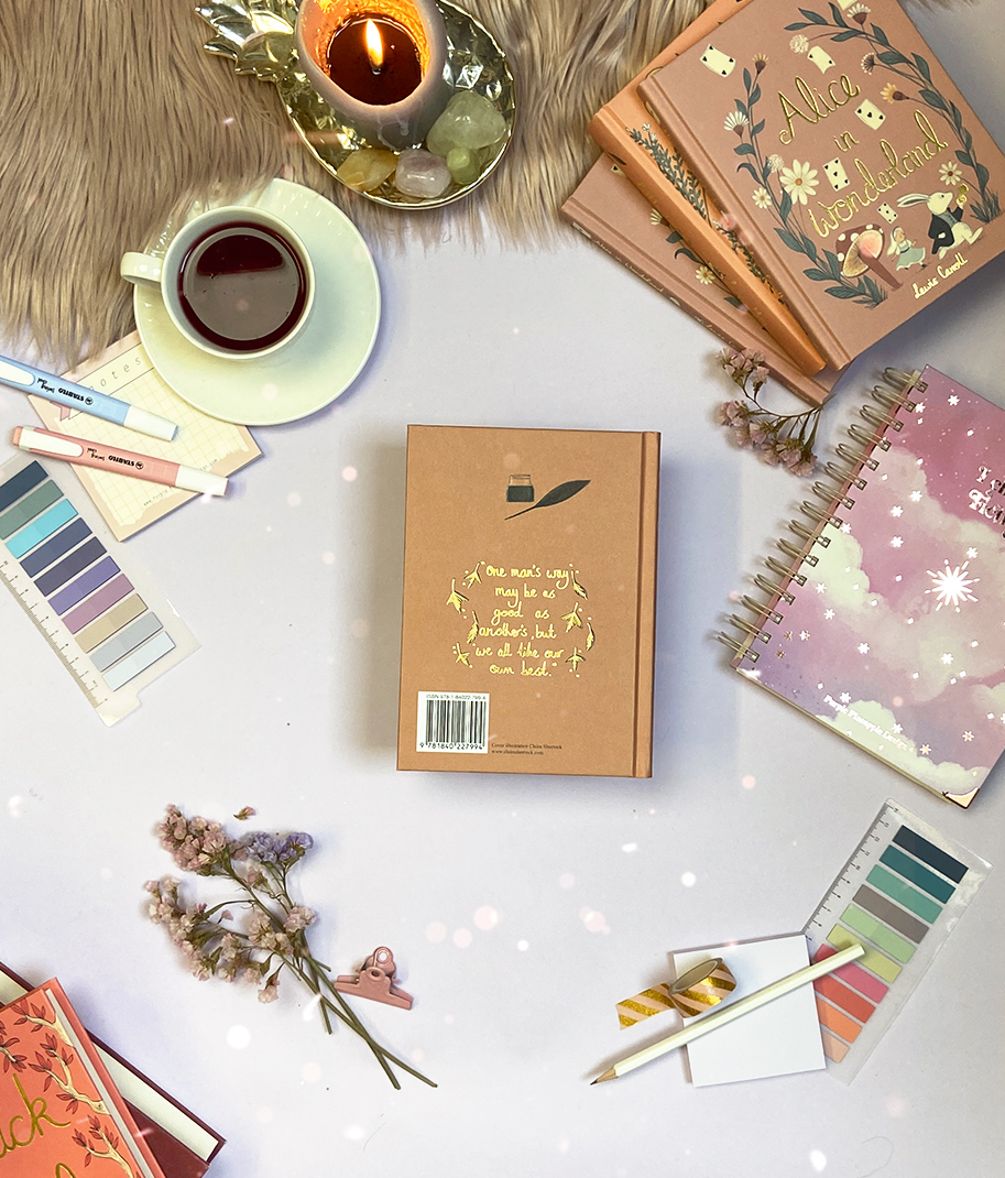 Vários cadernos, livros, paletas de cores, canetas, chávena com bebida e vela acesa sobre superfície clara com textura e tapete peludo