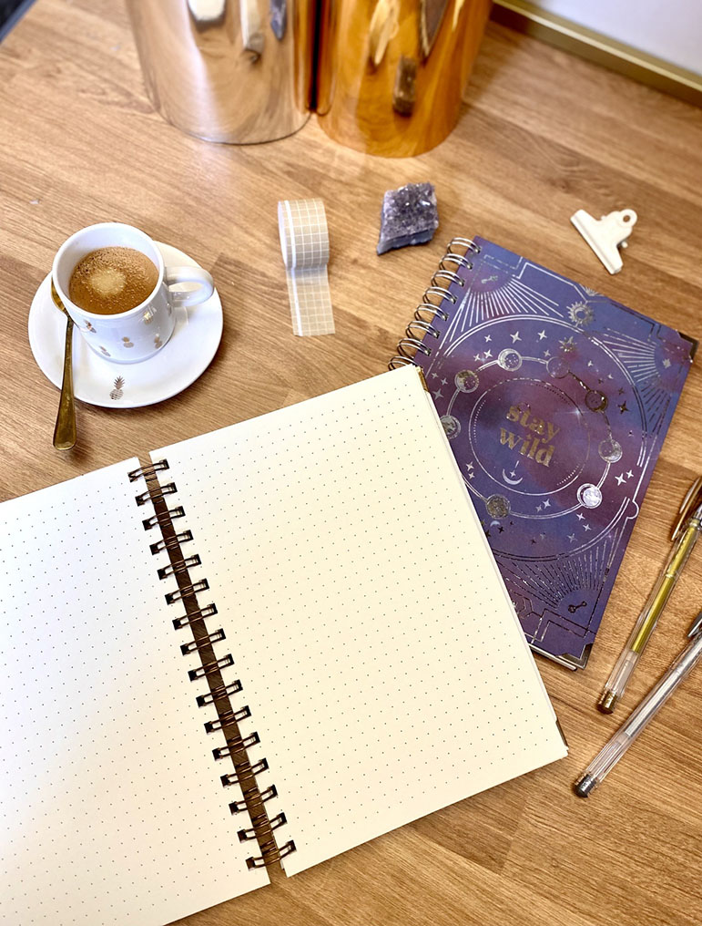 Mesa com cadernos, xícara de café, fita decorativa e frascos metálicos