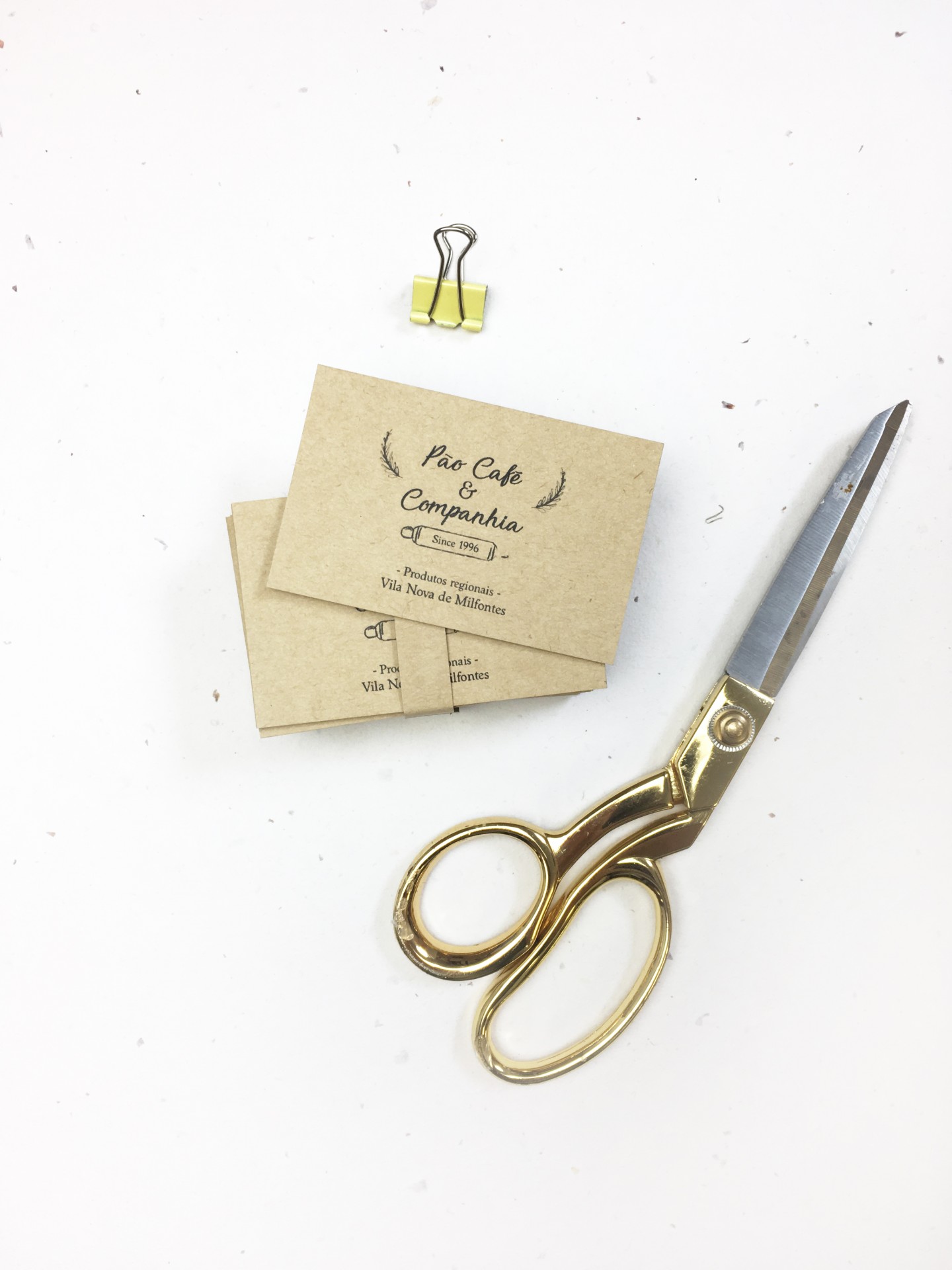 Tesouras douradas, clipe amarelo e cartões marrons com texto pretos sobre superfície branca