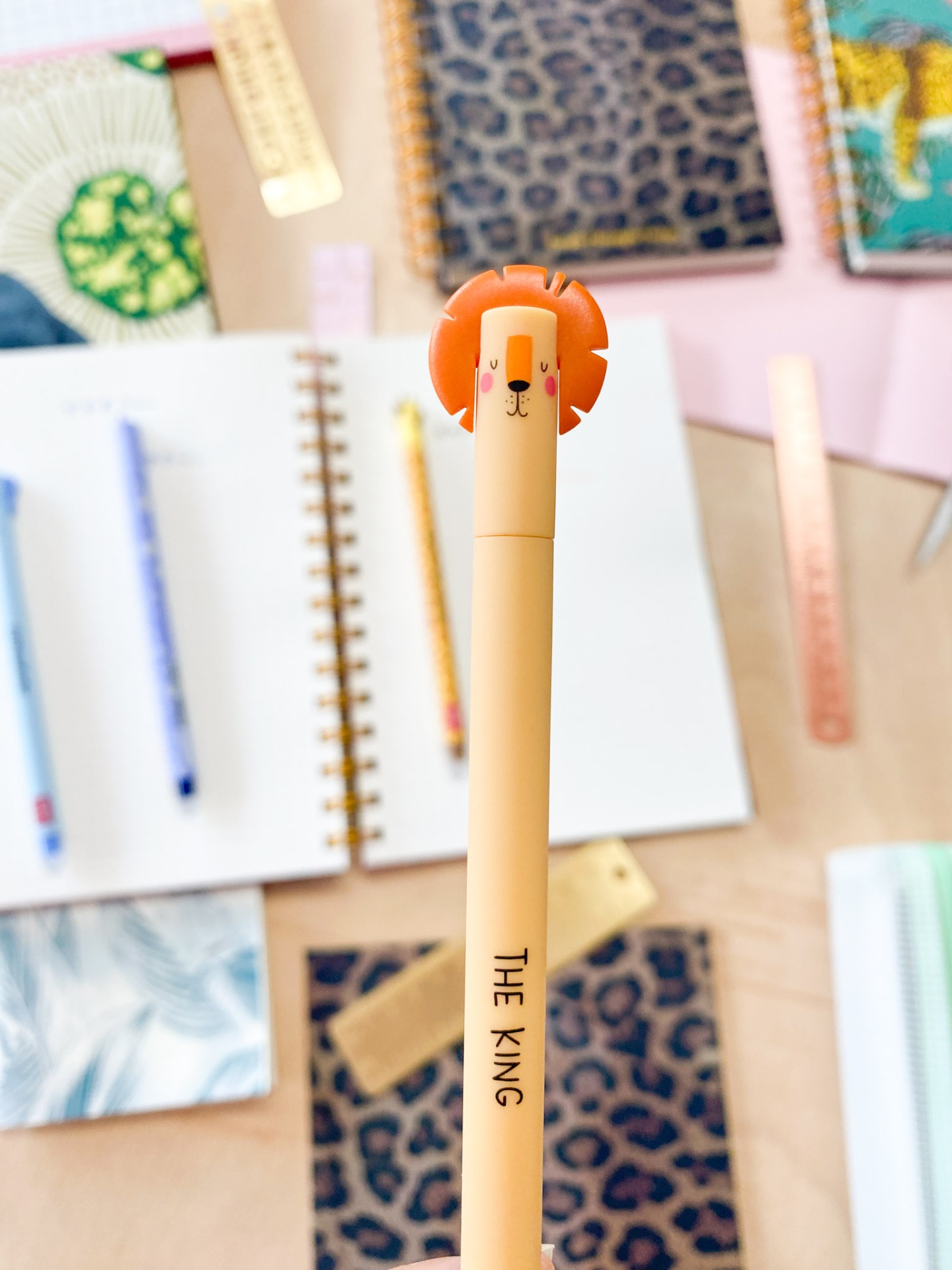 Caneta bege claro com figura de leão laranja na tampa e texto 'THE KING'